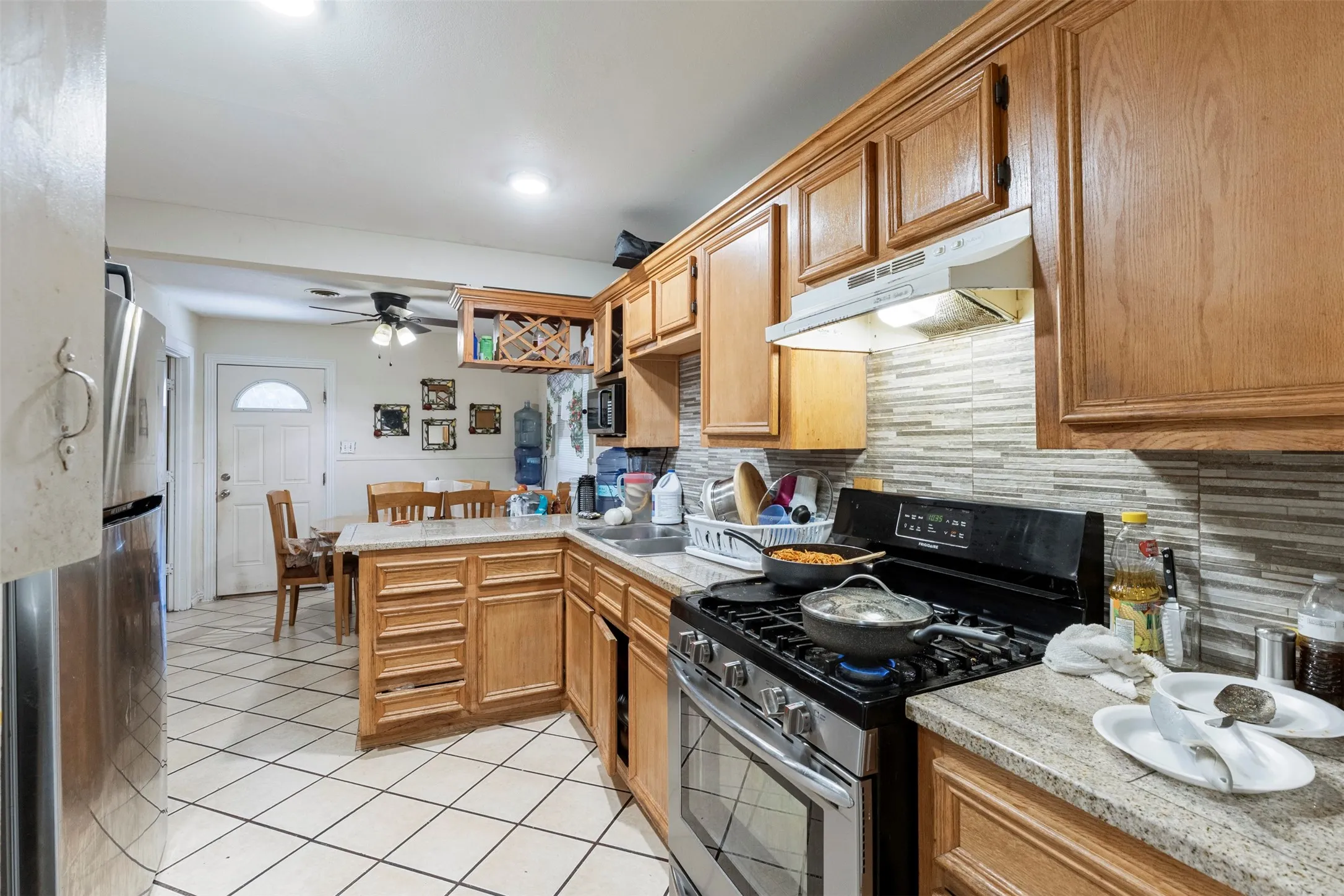 Kitchen featuring wood cabinetry, light-toned stone-finish countertops, and a full-height tile backsplash