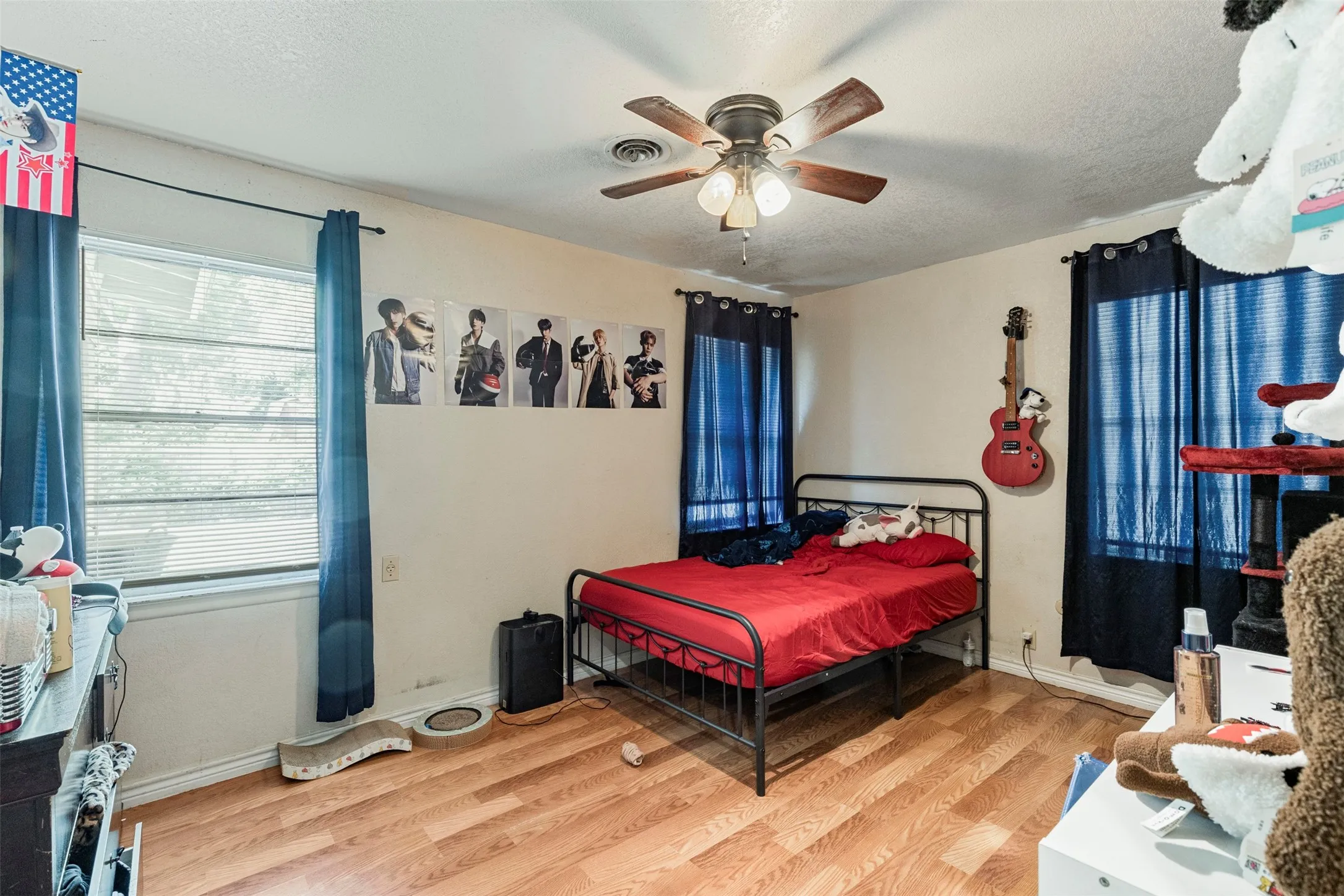 Room featuring wood-finish flooring, a ceiling fan with integrated lighting, and two windows with blinds and curtain rods