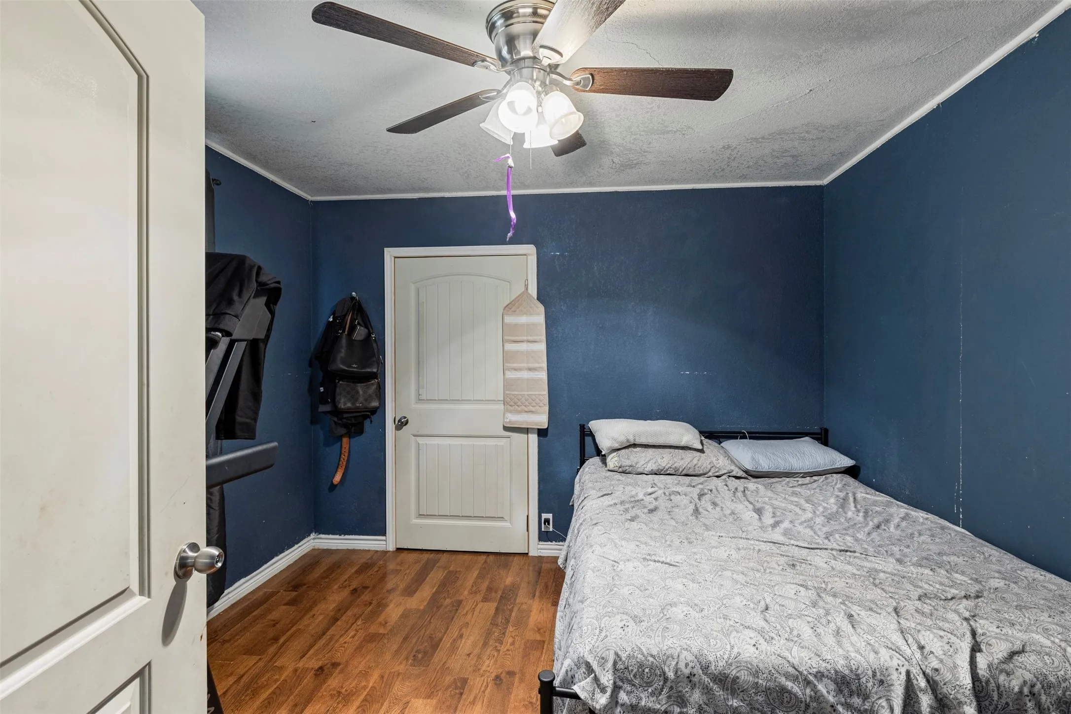 Room featuring rich blue walls, wood-finish flooring, a ceiling fan with integrated lighting, and white trim