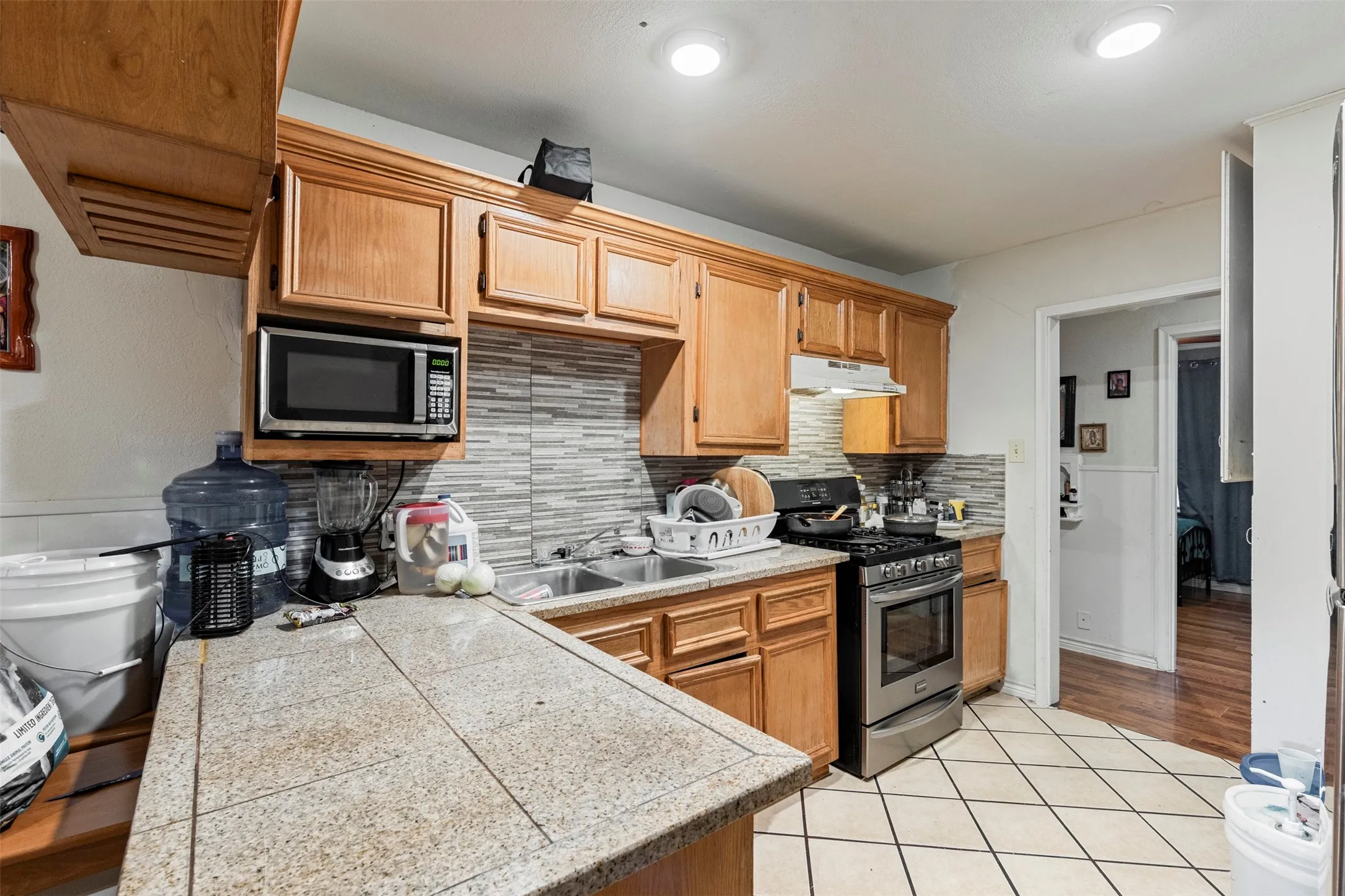 Kitchen featuring wood-finish cabinetry, tile countertops, a mosaic tile backsplash, stainless steel appliances, and recessed lighting