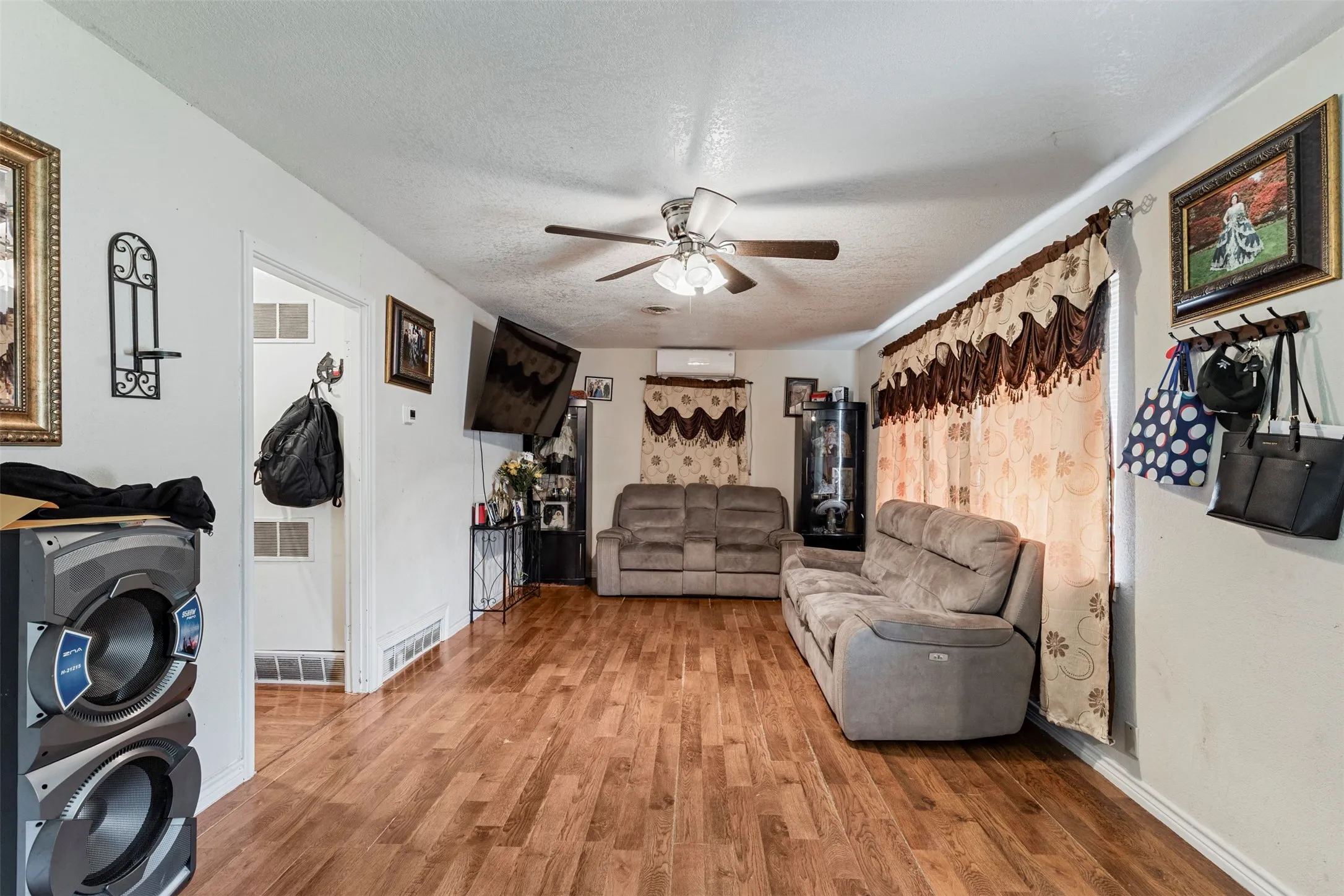 Spacious living area featuring wood-finish flooring, white walls, and a ceiling fan with integrated lighting