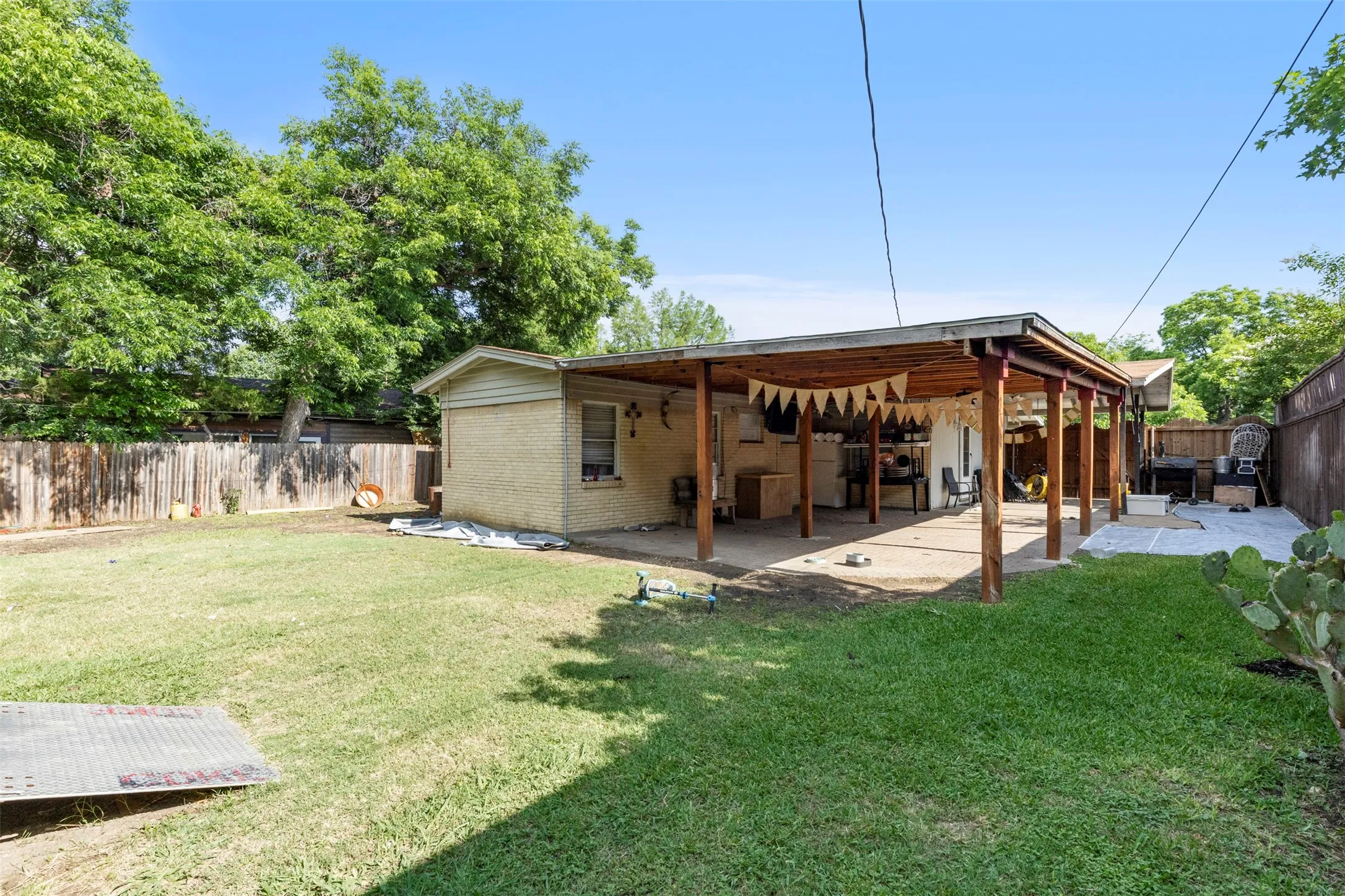 Expansive backyard featuring a covered patio with a wood beam structure, a large grassy area, a privacy fence, and mature trees