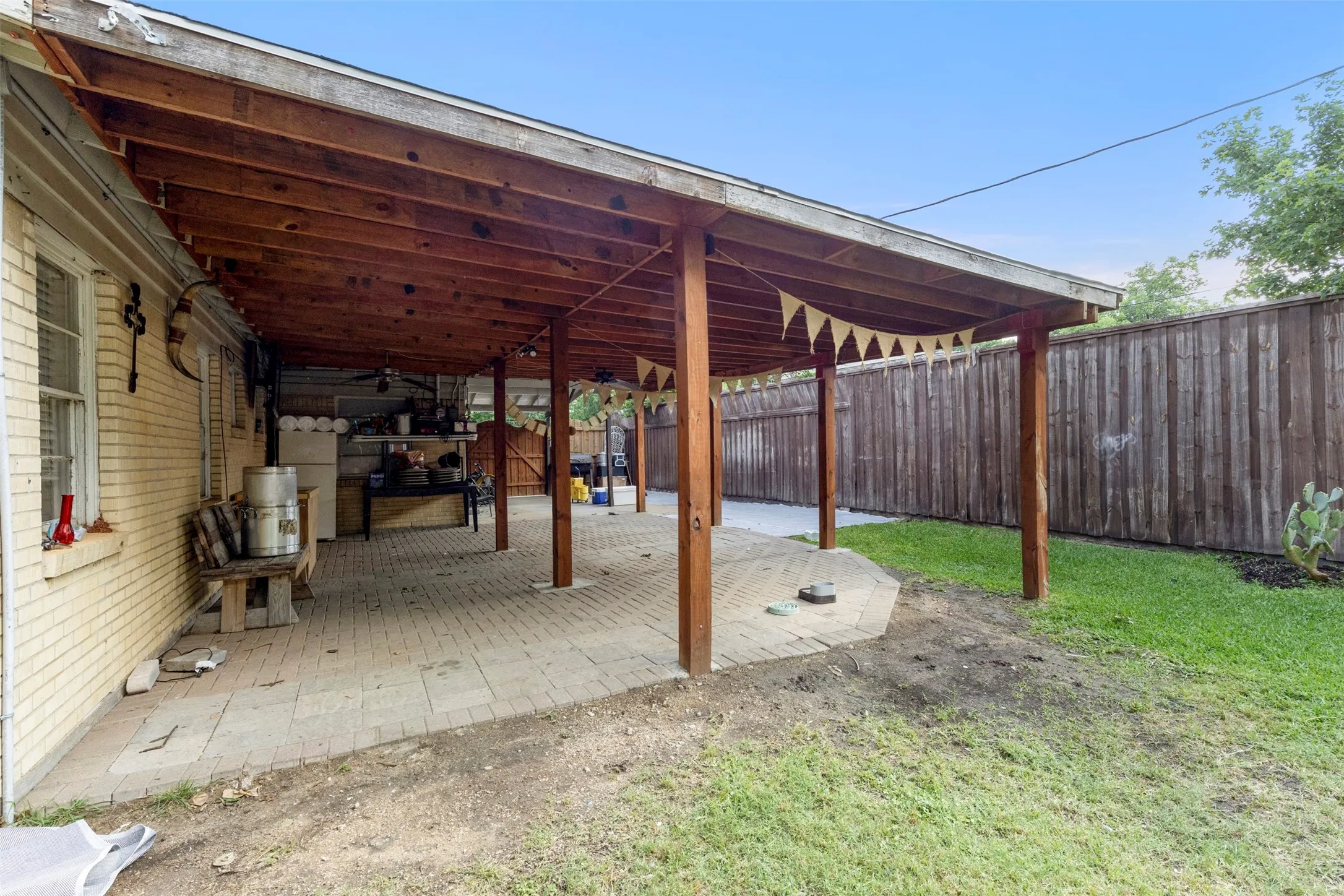 Expansive covered patio featuring a wood-beam ceiling, supporting columns, and paver flooring
