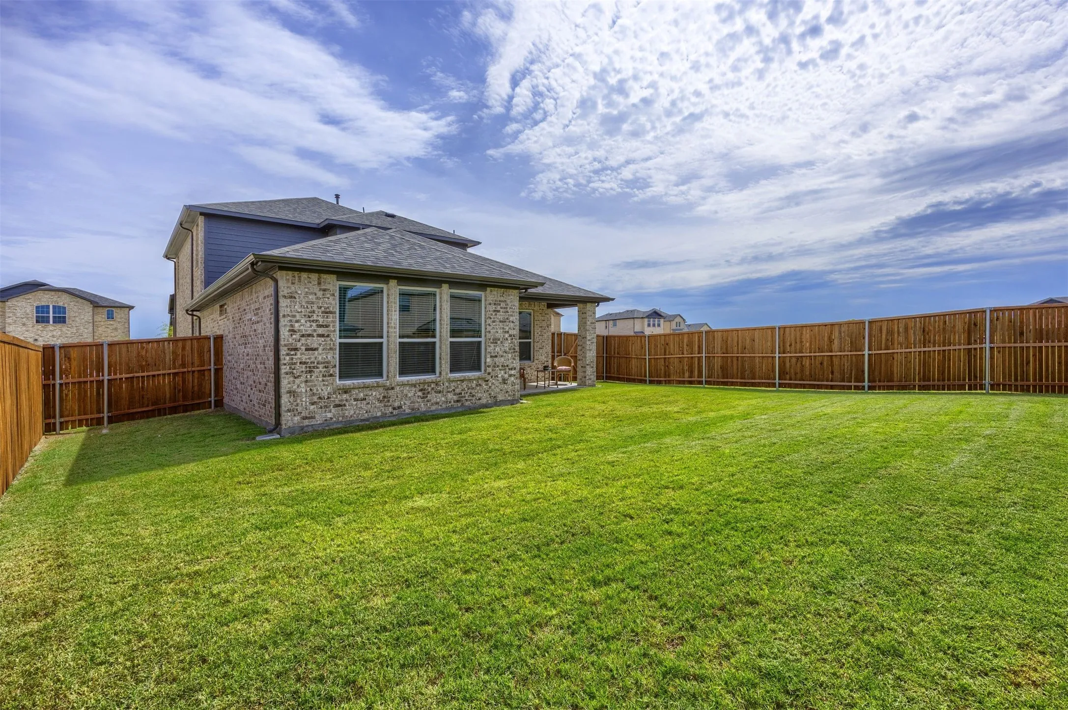 Expansive fenced backyard featuring a meticulously maintained lawn, a covered patio, and a brick exterior with multiple windows
