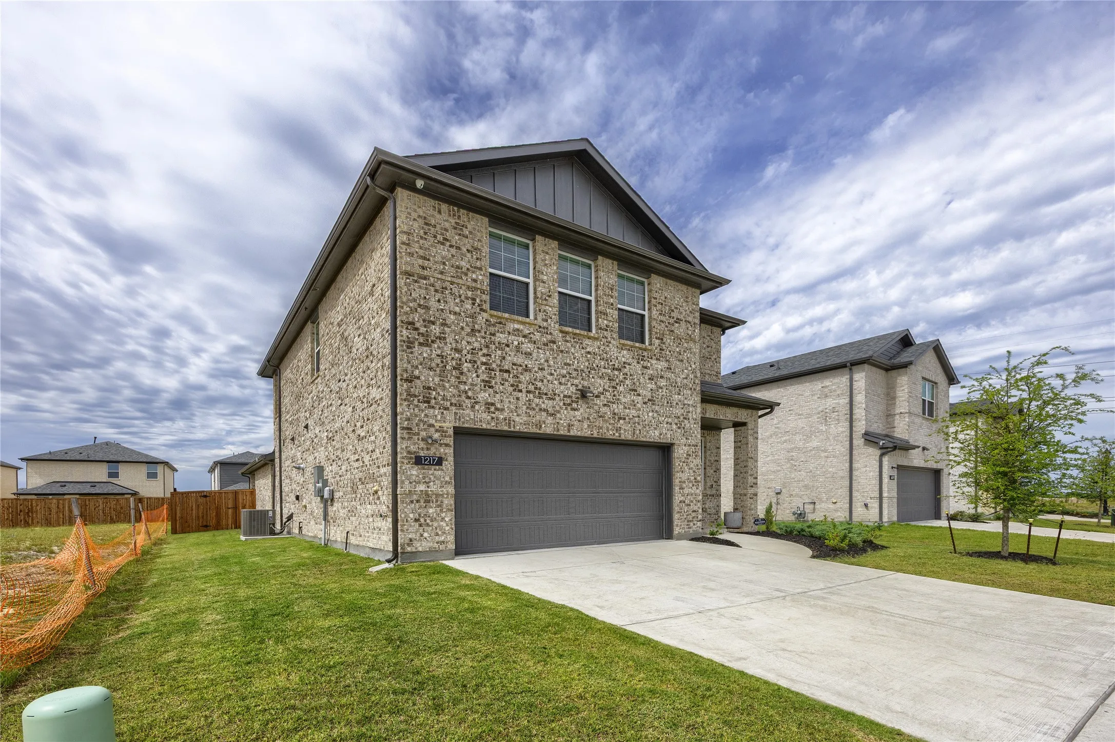 This view highlights the home's beautifully maintained, lush green yard and expansive, long concrete driveway. The side angle also showcases the generous extra spacing between properties, offering a wonderfully open and private setting.