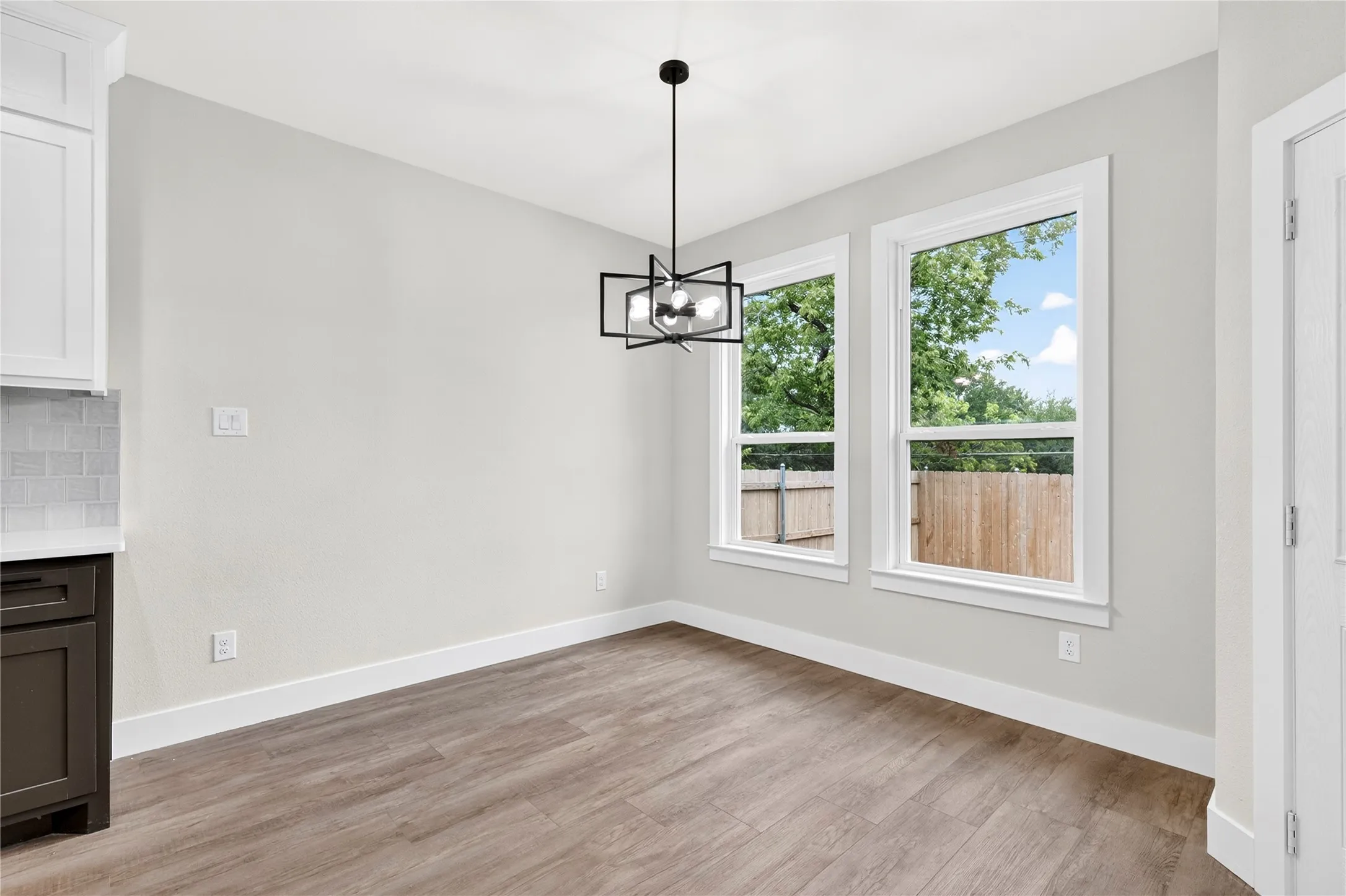 Dining area featuring wood-finish flooring, two large windows with white trim, a modern black geometric chandelier, and light gray walls
