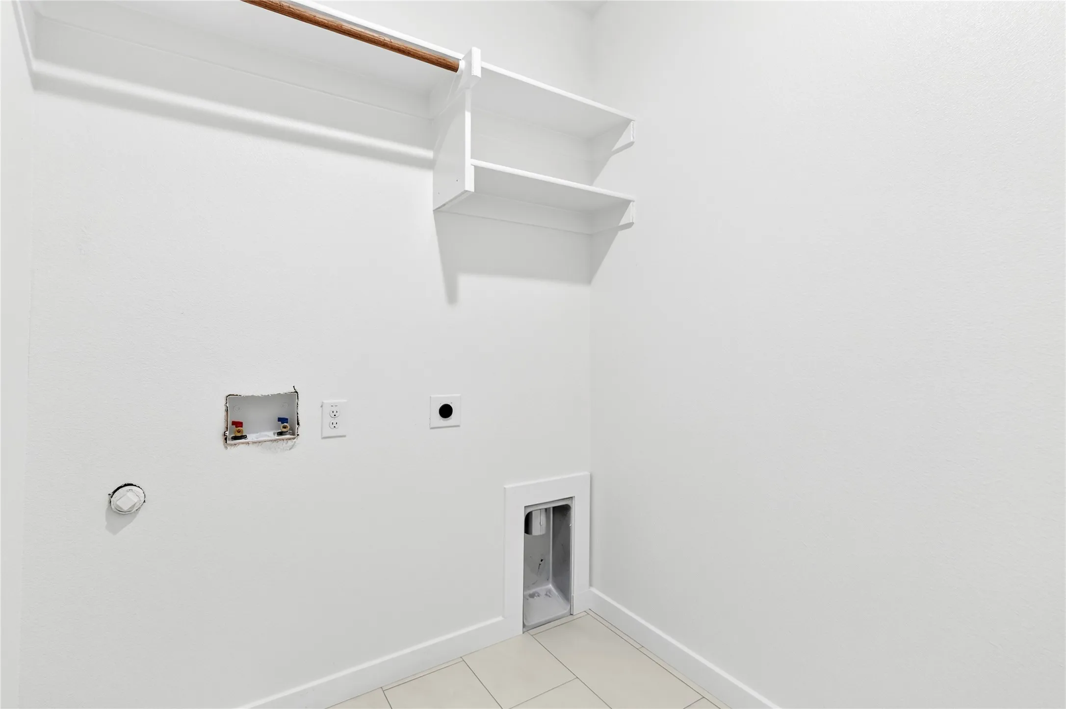 Dedicated laundry area featuring a built-in hanging rod, two upper storage shelves, washer and dryer hookups, and tiled flooring