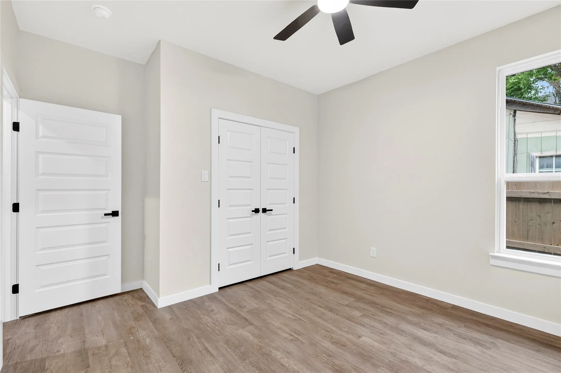 Bright room featuring wood-finish flooring, a white window frame, and a ceiling fan with integrated lighting