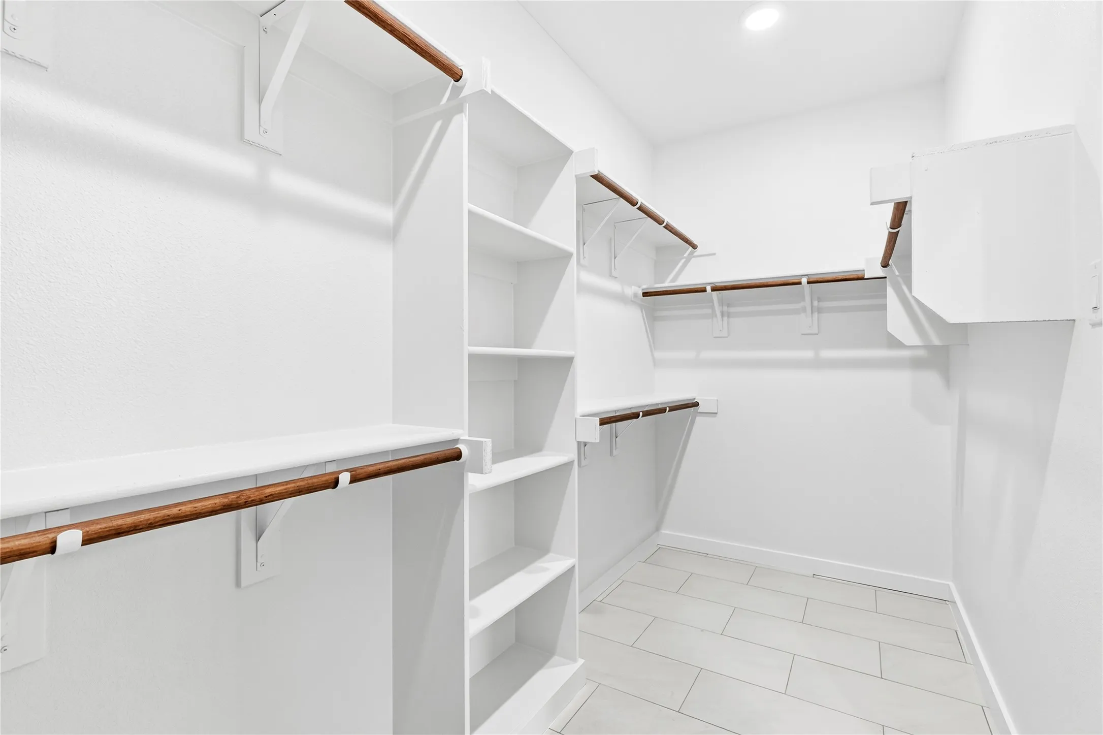 Walk-in closet featuring built-in shelving, multiple hanging rods, and light-toned tile flooring