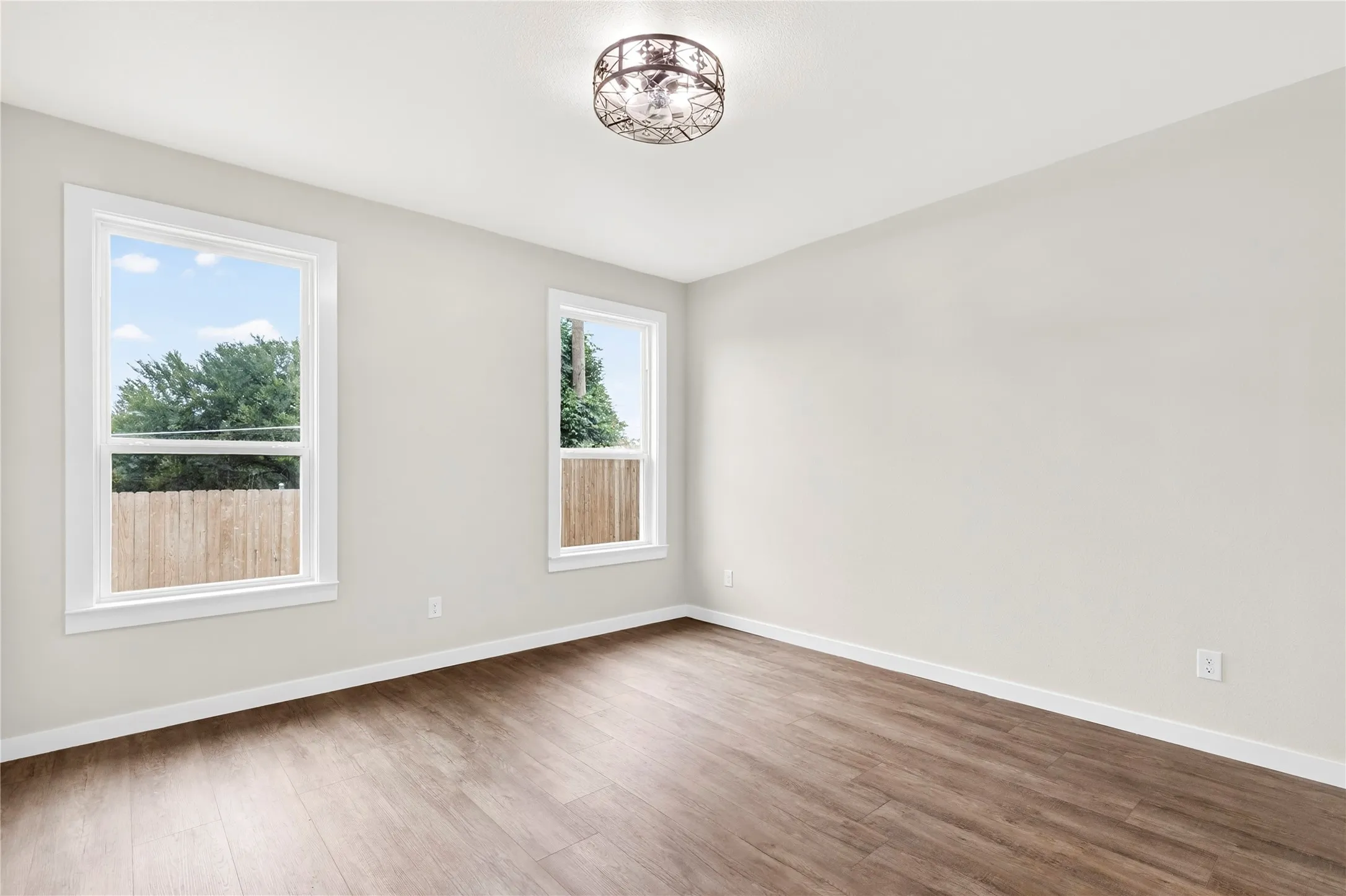 Bright room featuring two large windows, wood-finish flooring, light neutral wall tones, white trim, and an ornate ceiling light fixture