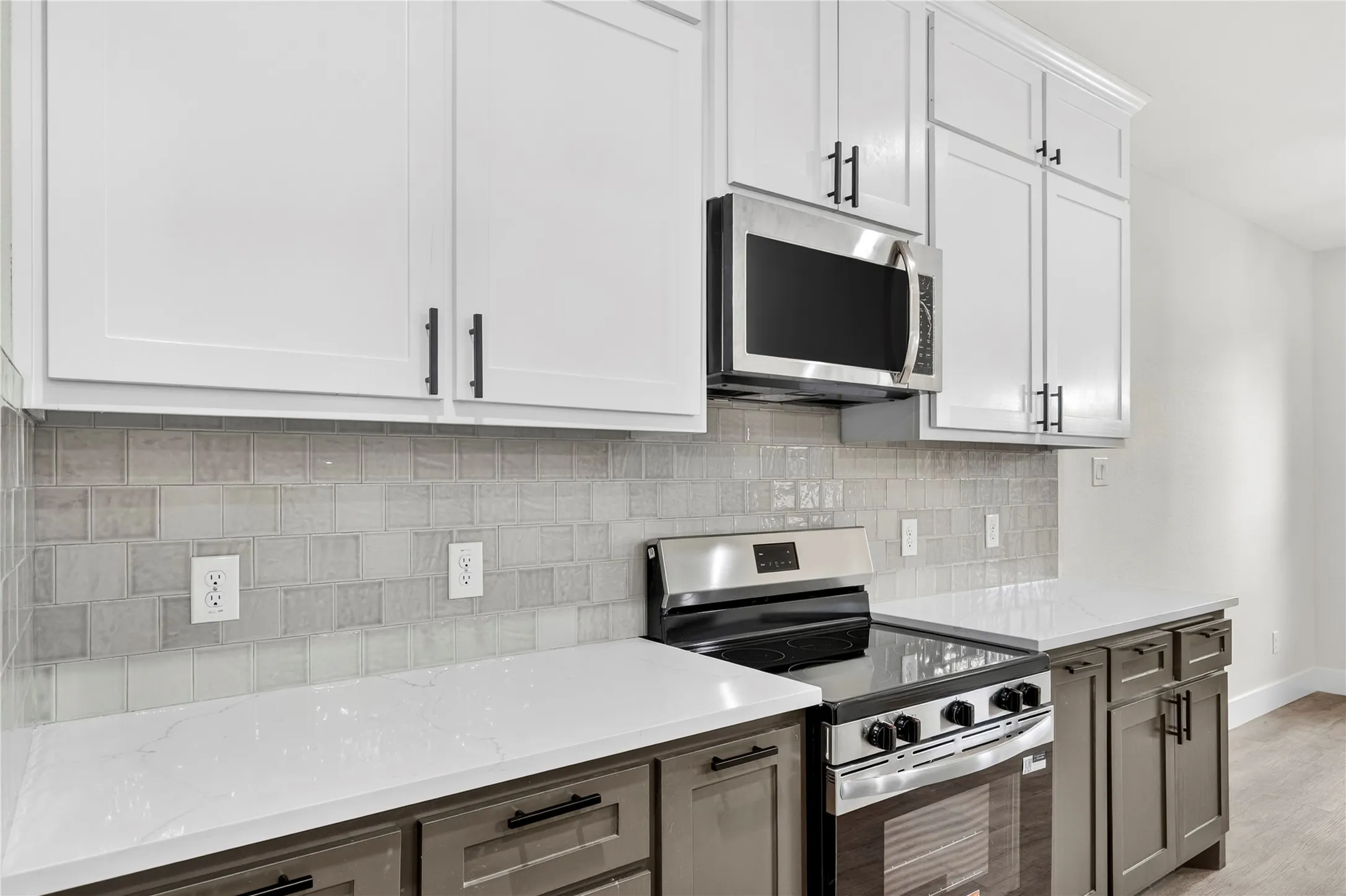 Kitchen featuring two-tone cabinetry with matte black hardware, white countertops, a mosaic tile backsplash, stainless steel microwave, and stainless steel range