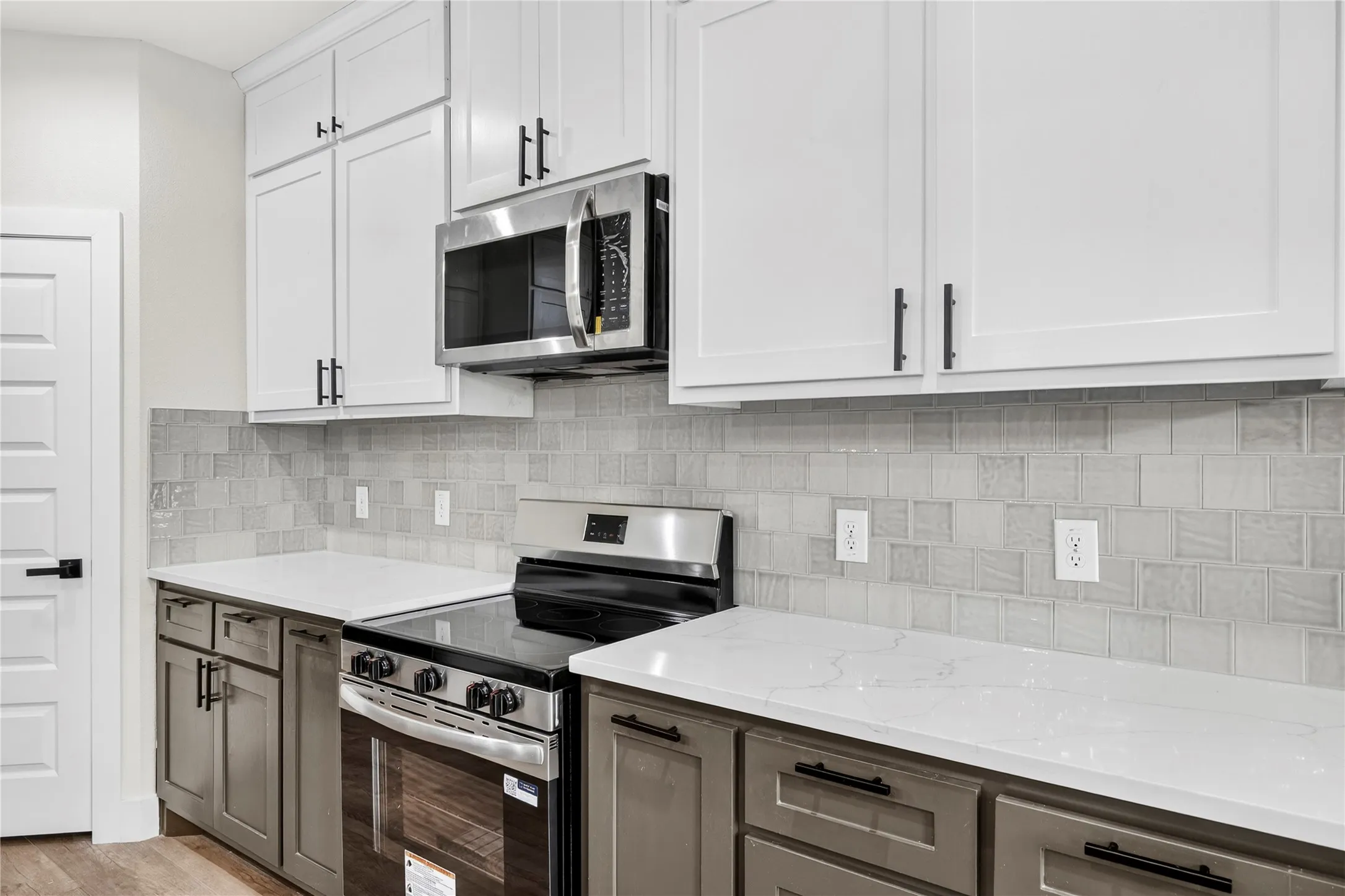 Contemporary kitchen featuring two-tone cabinetry with white upper and grey lower units, stainless steel microwave, and a black and stainless steel range