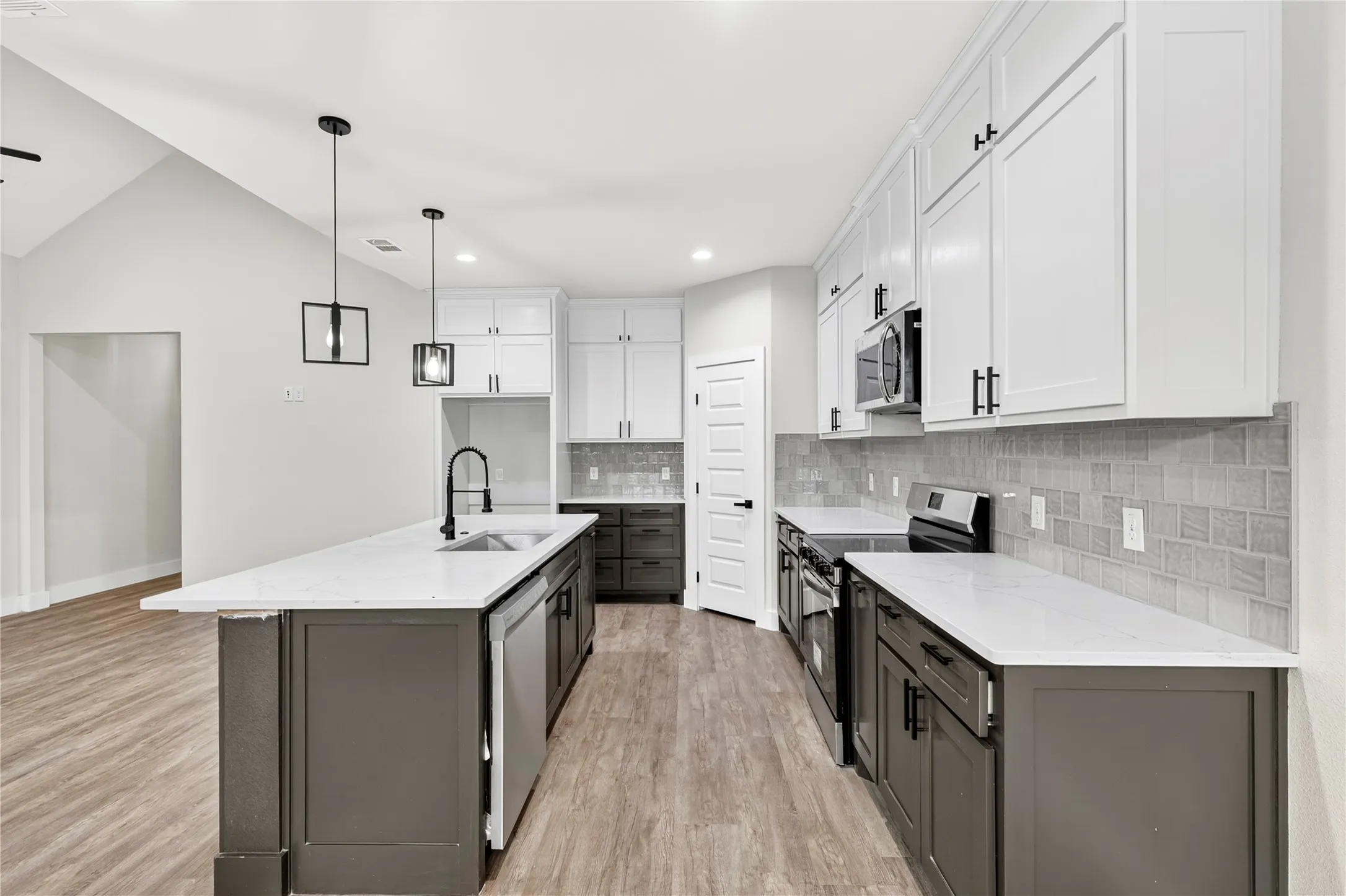 Modern kitchen featuring wood-finish flooring, two-tone cabinetry with white upper and dark lower units, white countertops, and a tiled backsplash