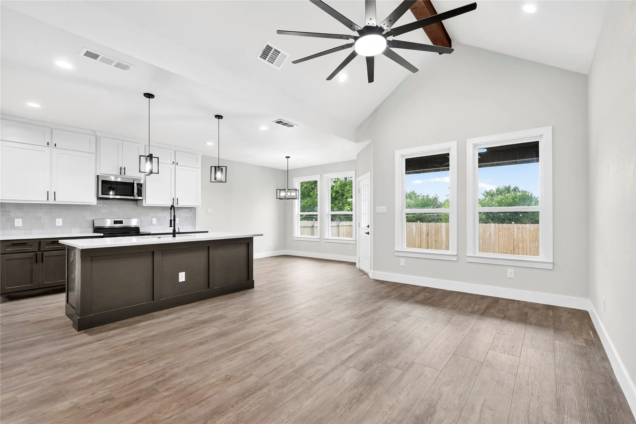 Open-concept living space featuring wood-finish flooring, a vaulted ceiling with a ceiling fan, and multiple windows