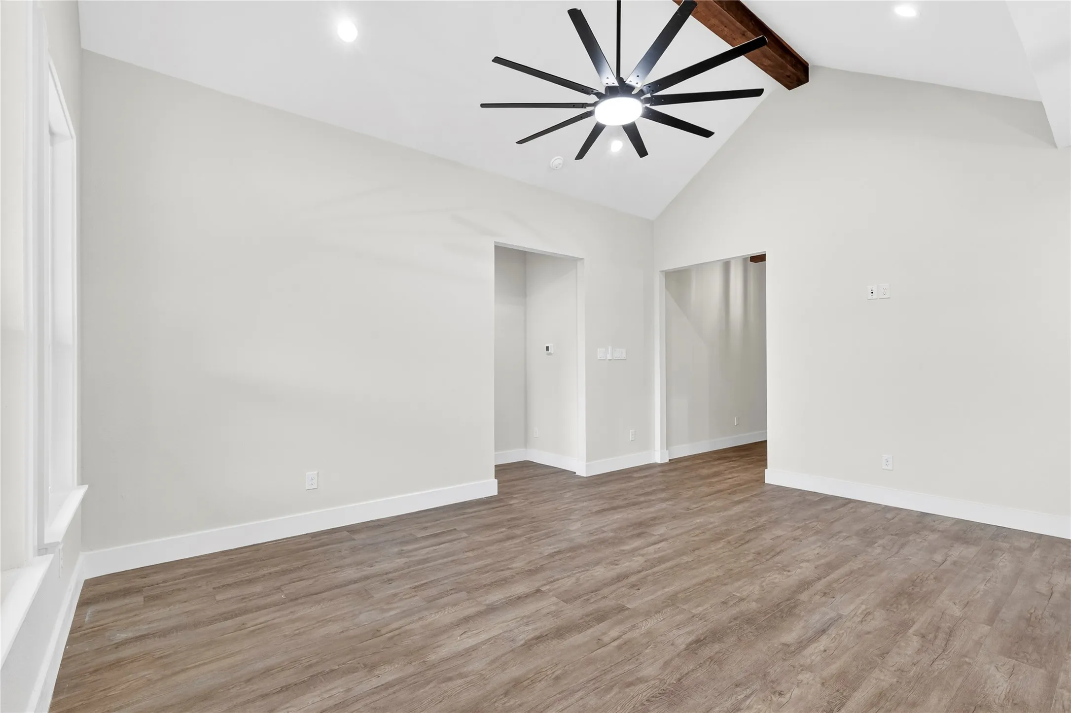 Spacious interior room featuring vaulted ceilings, a prominent exposed wood beam, and a modern ceiling fan with multiple blades