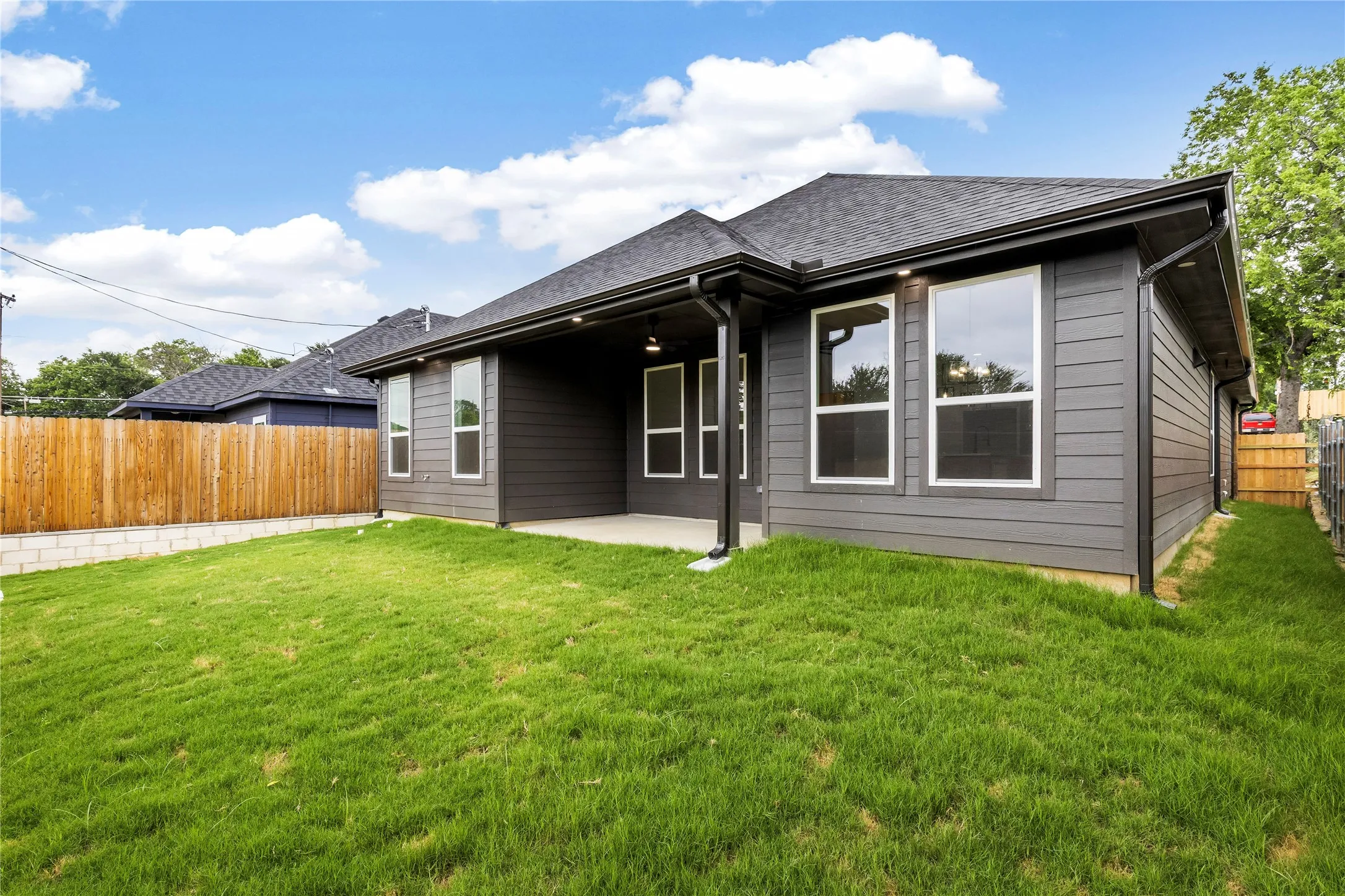 Modern siding exterior with multiple large windows, a covered patio, and a spacious green lawn
