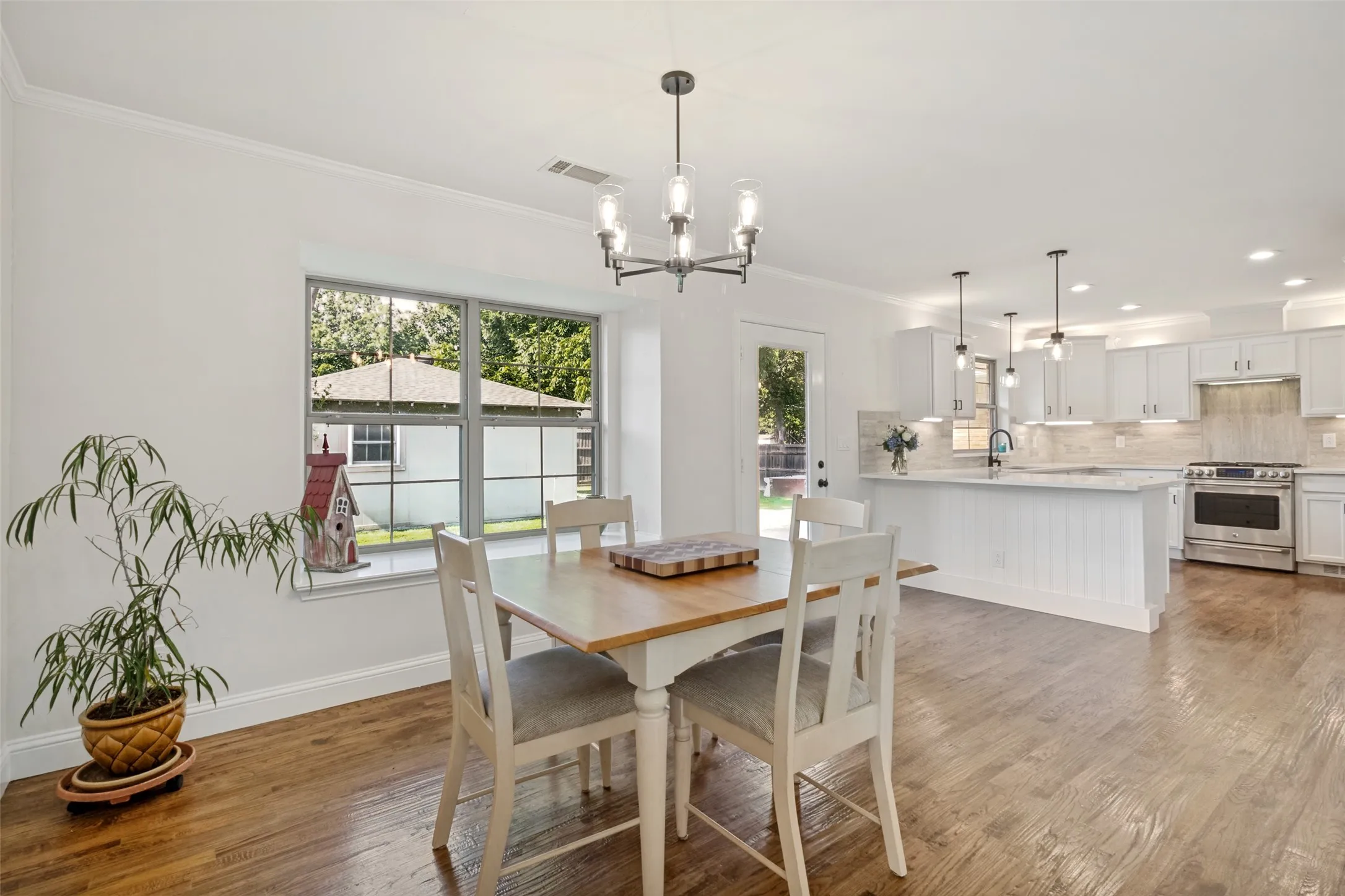 Open-concept interior featuring wood flooring, a contemporary chandelier, a large window, a kitchen island with beadboard trim, and a stainless steel range