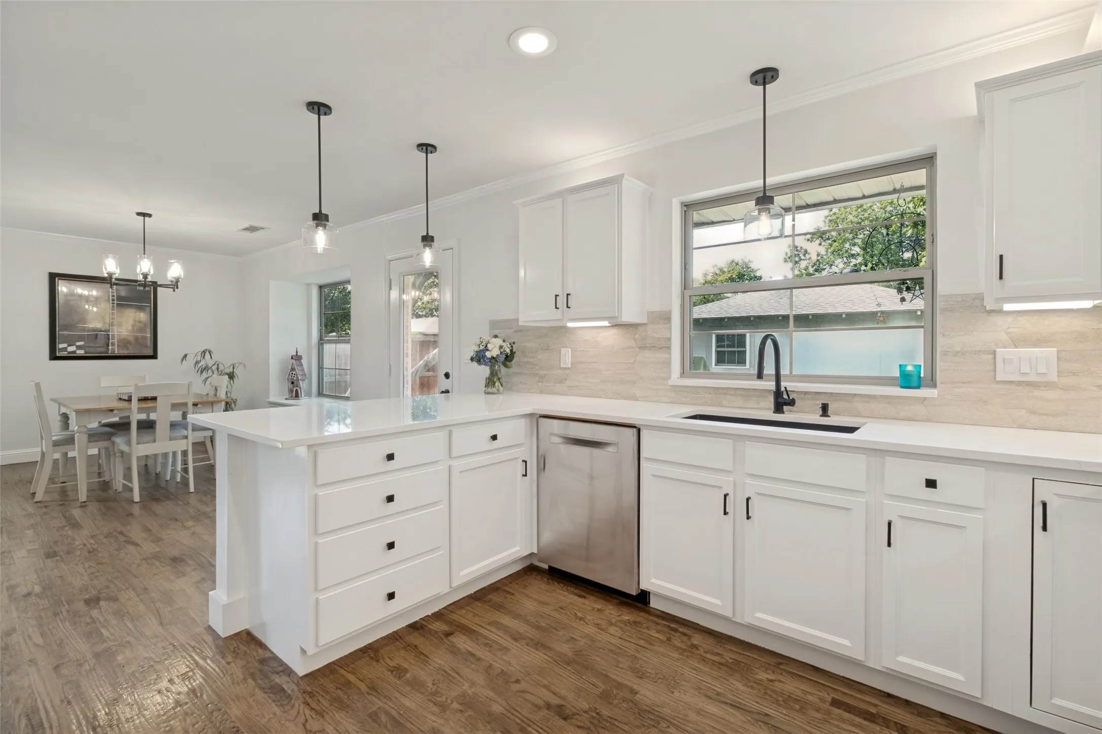 Bright kitchen featuring white shaker cabinetry, stainless steel dishwasher, and wood flooring