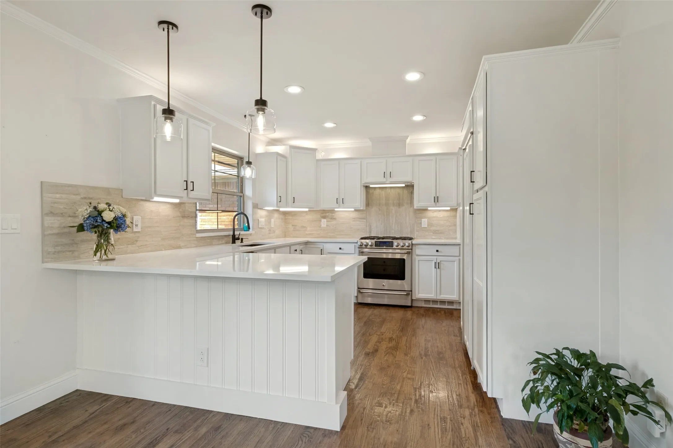 Modern kitchen featuring white shaker cabinetry, stainless steel range, quartz countertops, and wood flooring