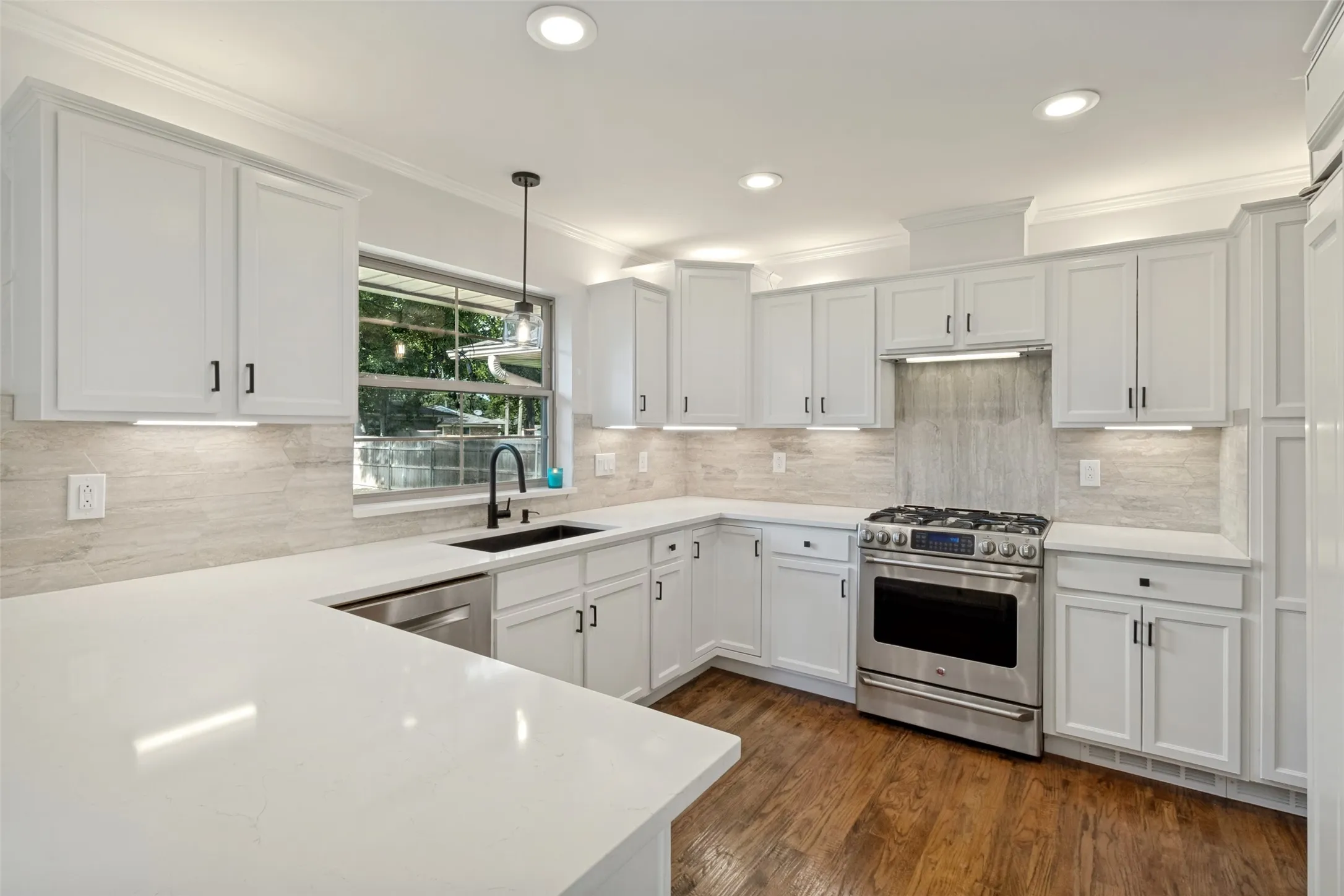 Modern kitchen featuring white shaker cabinetry, stainless steel appliances, light-toned tiled backsplash, recessed lighting, and wood flooring