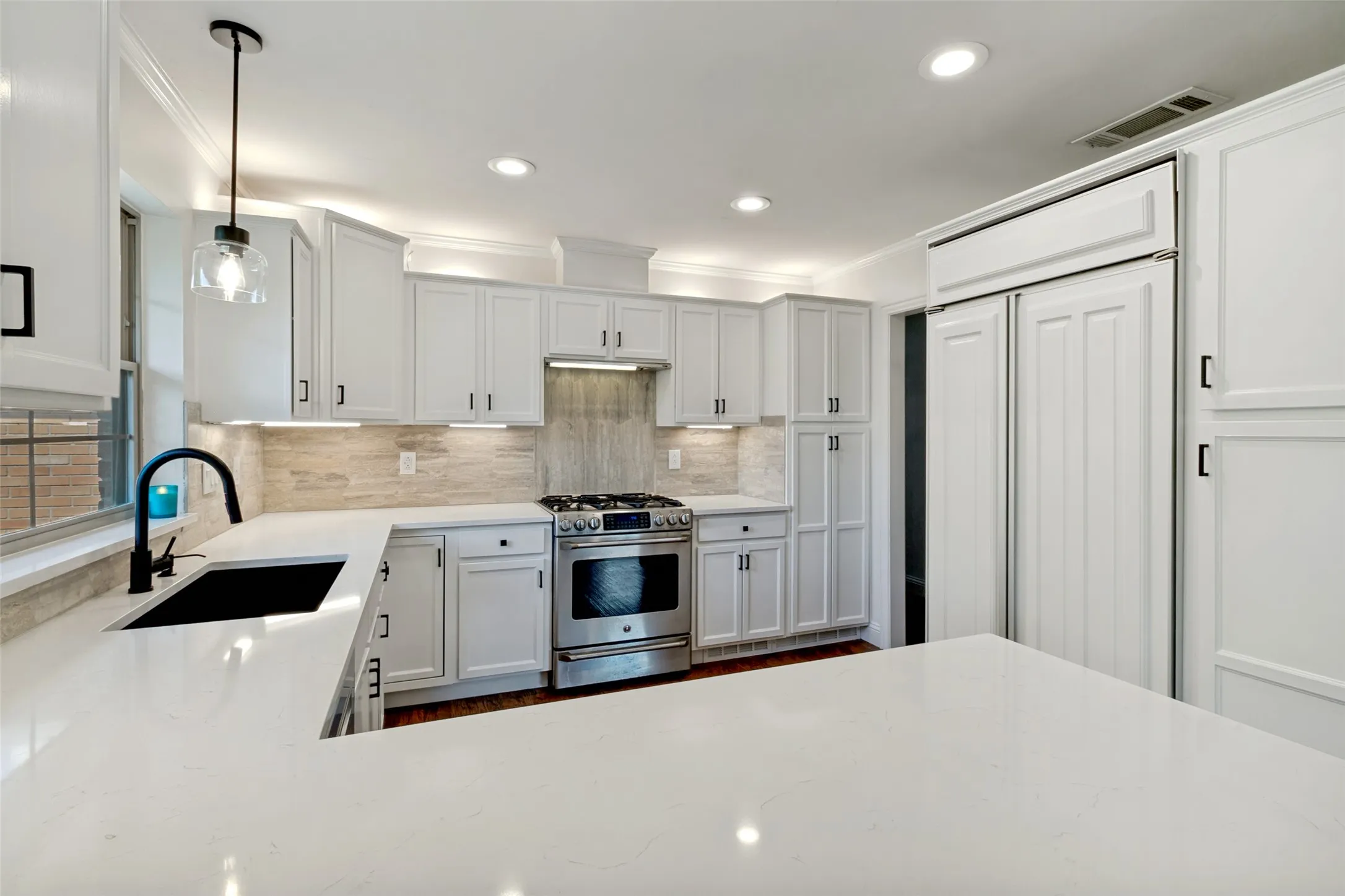 Kitchen featuring white shaker-style cabinetry, a built-in stainless steel range, white countertops, a black sink with a matte black faucet, and a stone tile backsplash