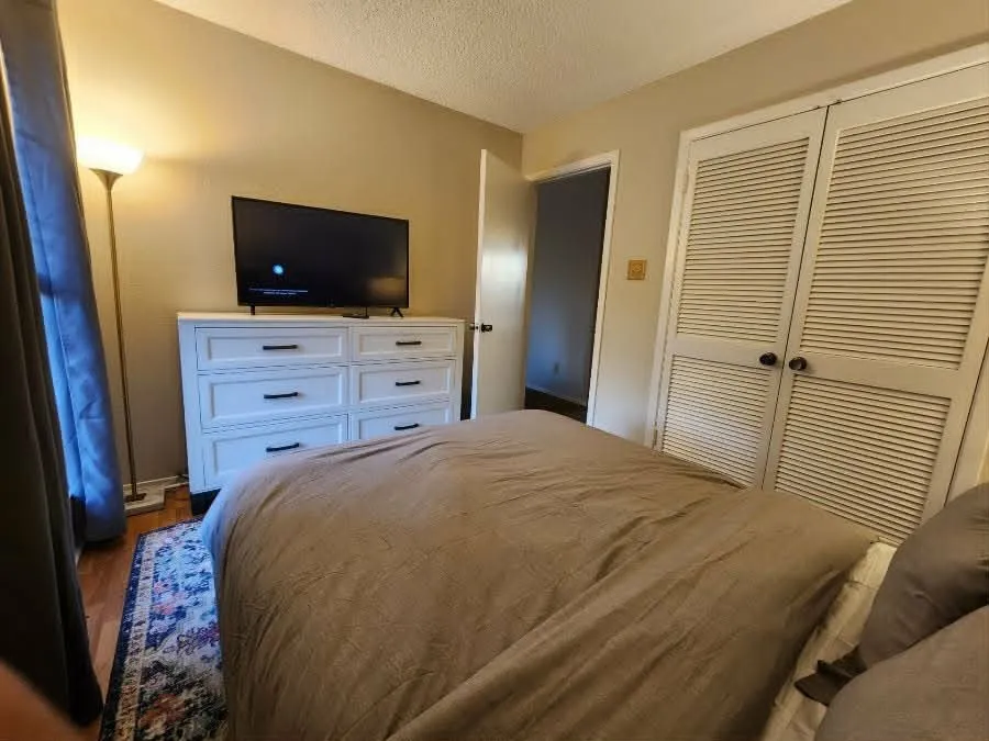 Wood-finish flooring with an area rug, louvered bi-fold closet doors, and neutral wall paint