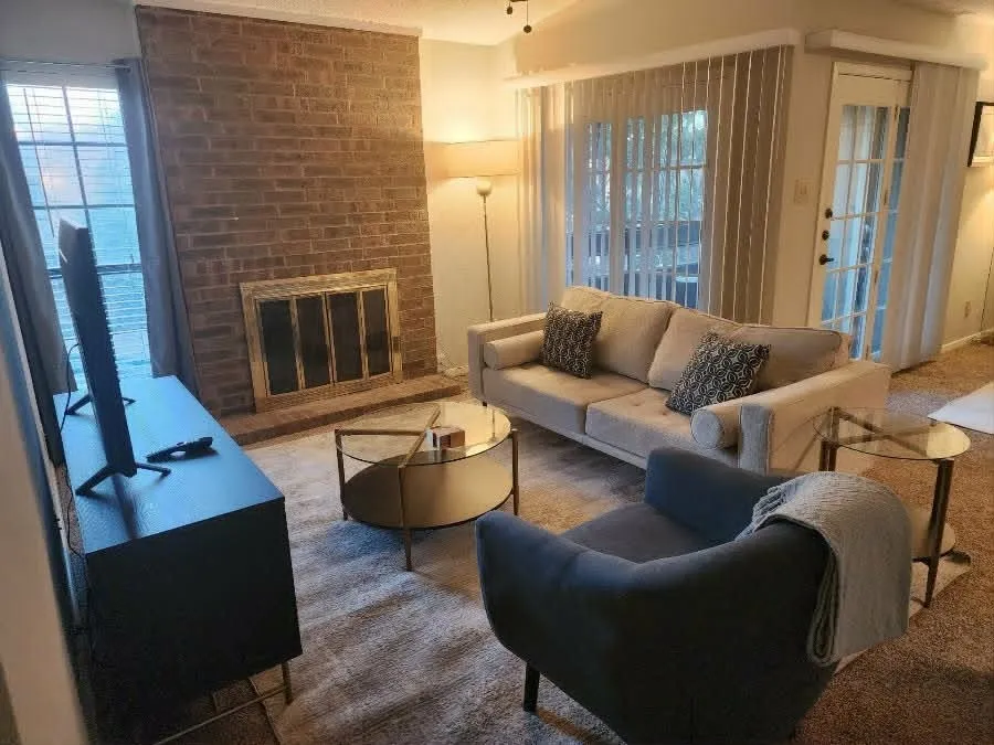 Living area featuring a brick fireplace with a brass-toned fire screen, textured carpeting, and a glass-paned door