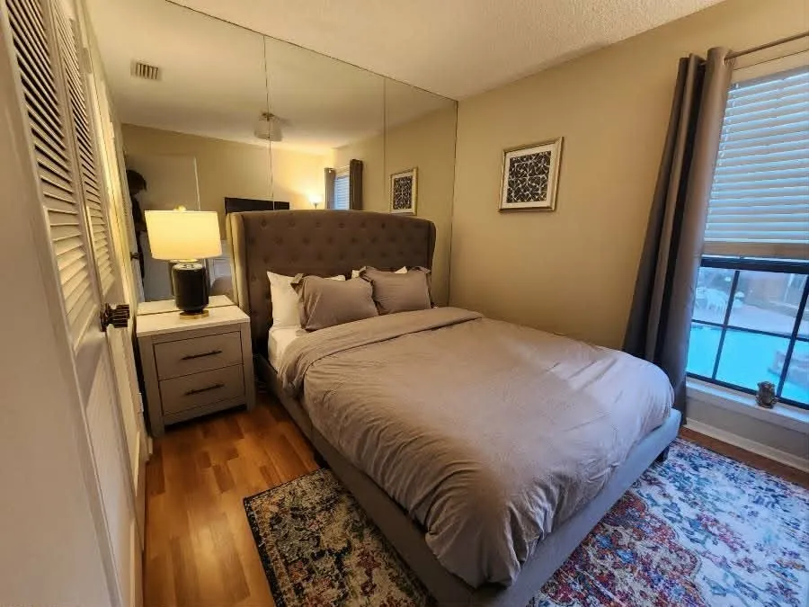 Wood-finish flooring throughout, complemented by a large window with privacy blinds, and a mirrored wall