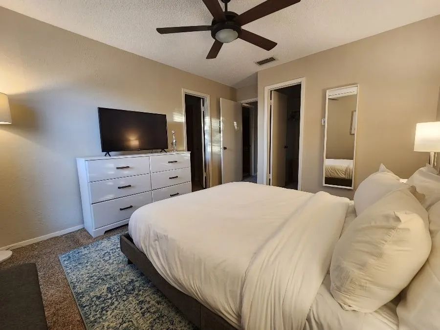 Carpeted room with a ceiling fan, two doorways, and a wall-mounted mirror