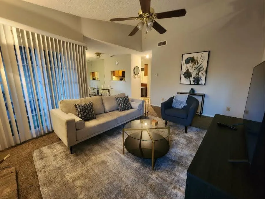 Living area featuring vaulted ceilings, a ceiling fan, and vertical blinds on the large window