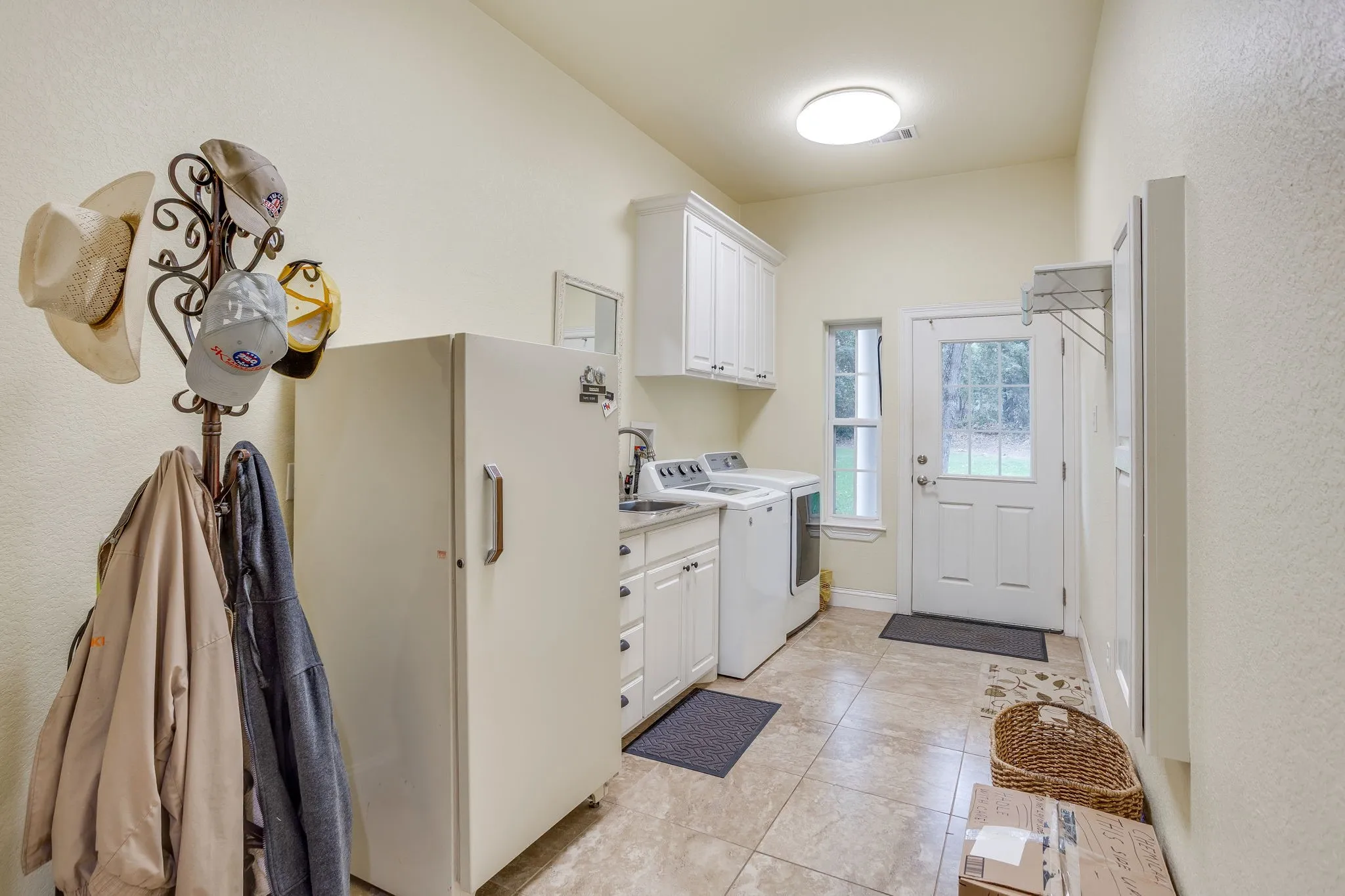 Utility room with tile flooring, white cabinetry, a sink, and an exterior door with a glass pane