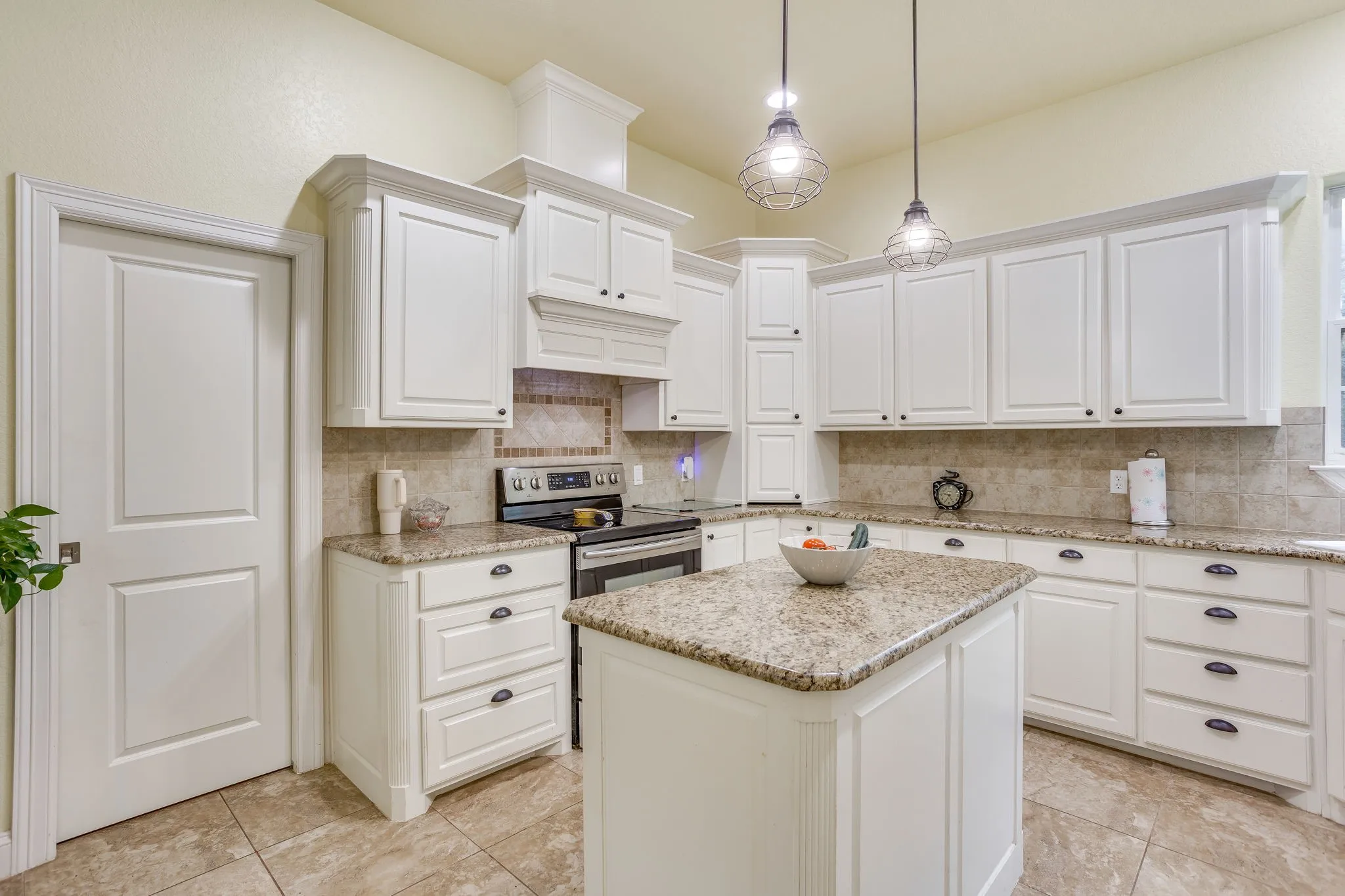 Kitchen featuring white cabinetry, a central island with a stone countertop, tile flooring, and two pendant light fixtures