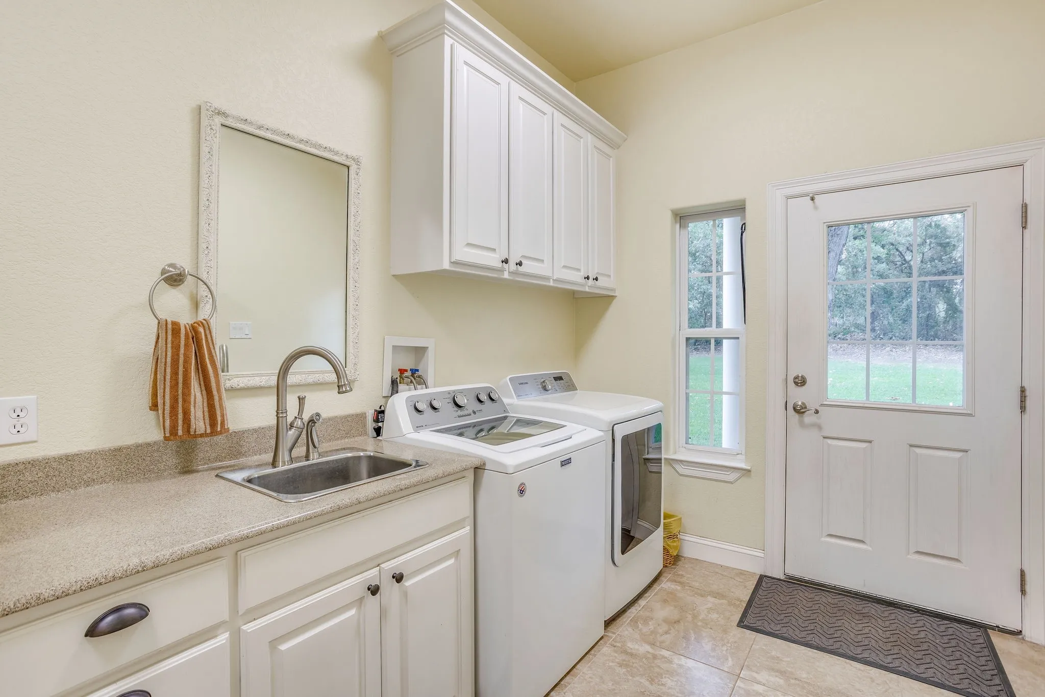 Laundry room featuring a utility sink with a gooseneck faucet, light-toned countertop, and white cabinetry