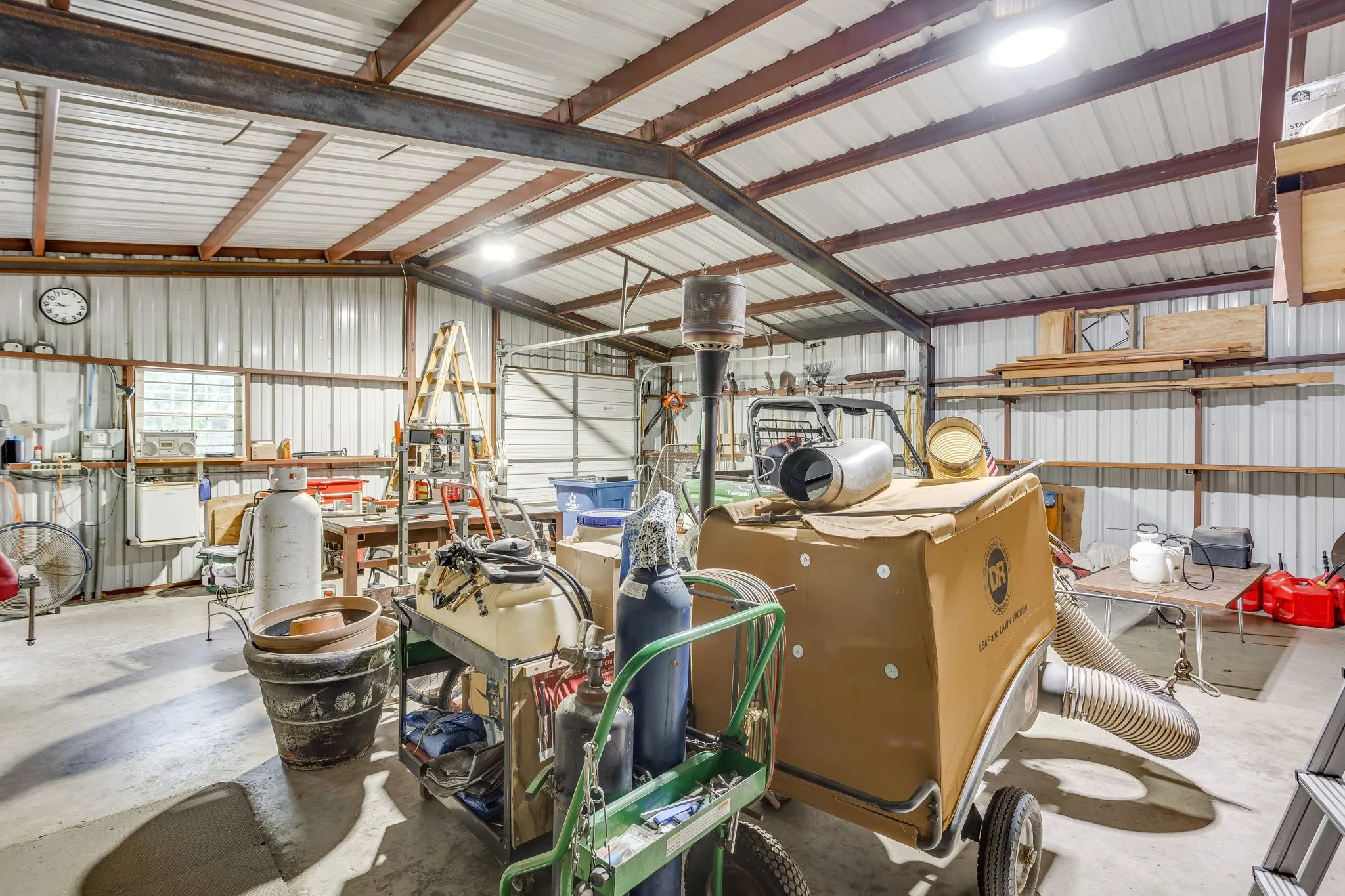 Spacious metal building featuring a corrugated metal roof, exposed structural beams, corrugated metal walls, concrete flooring, and multiple ceiling-mounted light fixtures