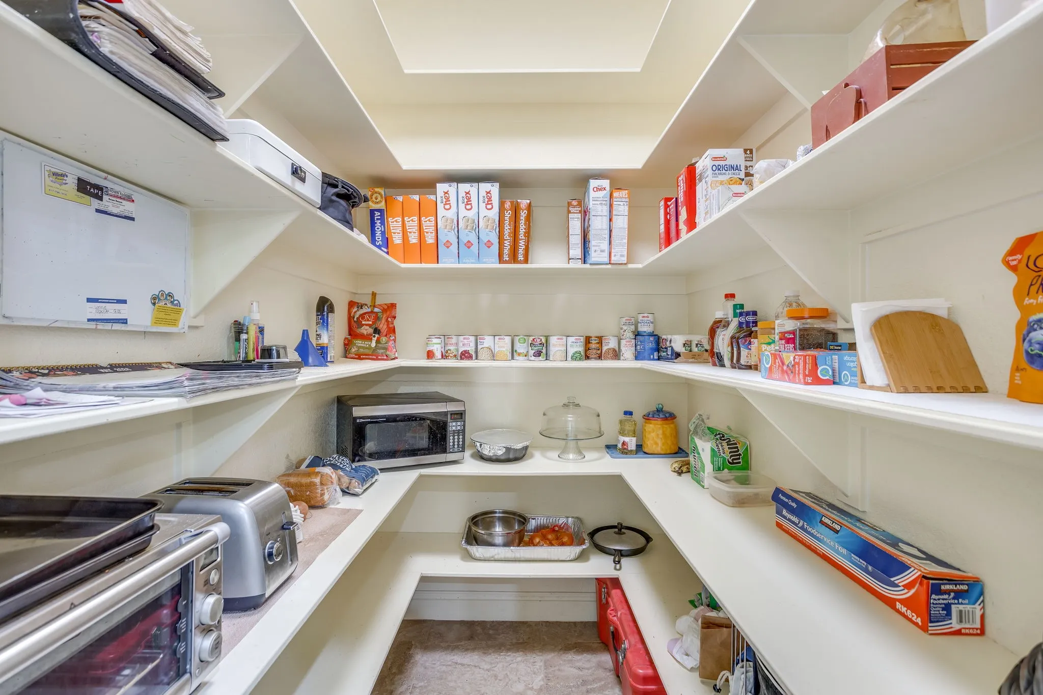 Spacious walk-in pantry featuring extensive built-in shelving, a skylight, and durable surface flooring