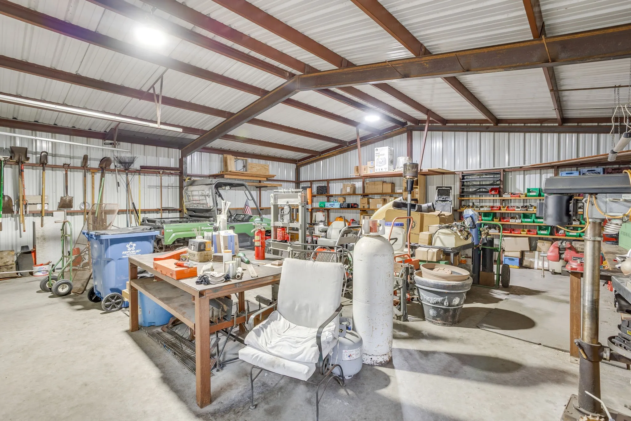 Spacious metal building featuring a concrete floor, exposed metal beam ceiling, corrugated metal walls, and overhead lighting