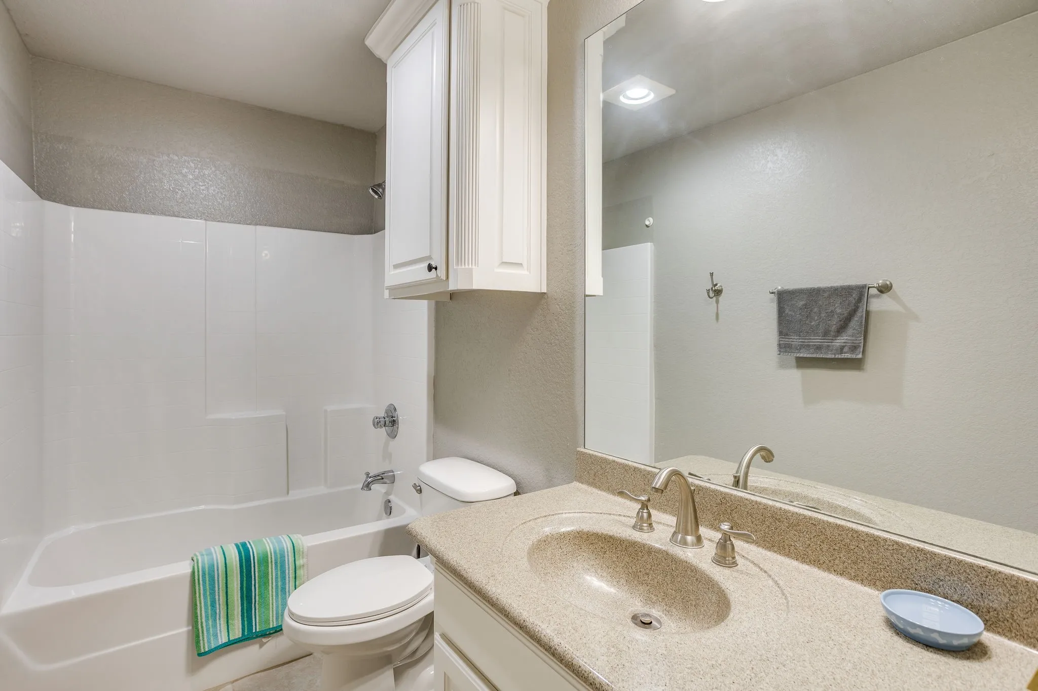 Bathroom featuring a neutral color palette, a full vanity with an integrated sink and countertop, a chrome faucet, a large mirror, and a white tub with a shower
