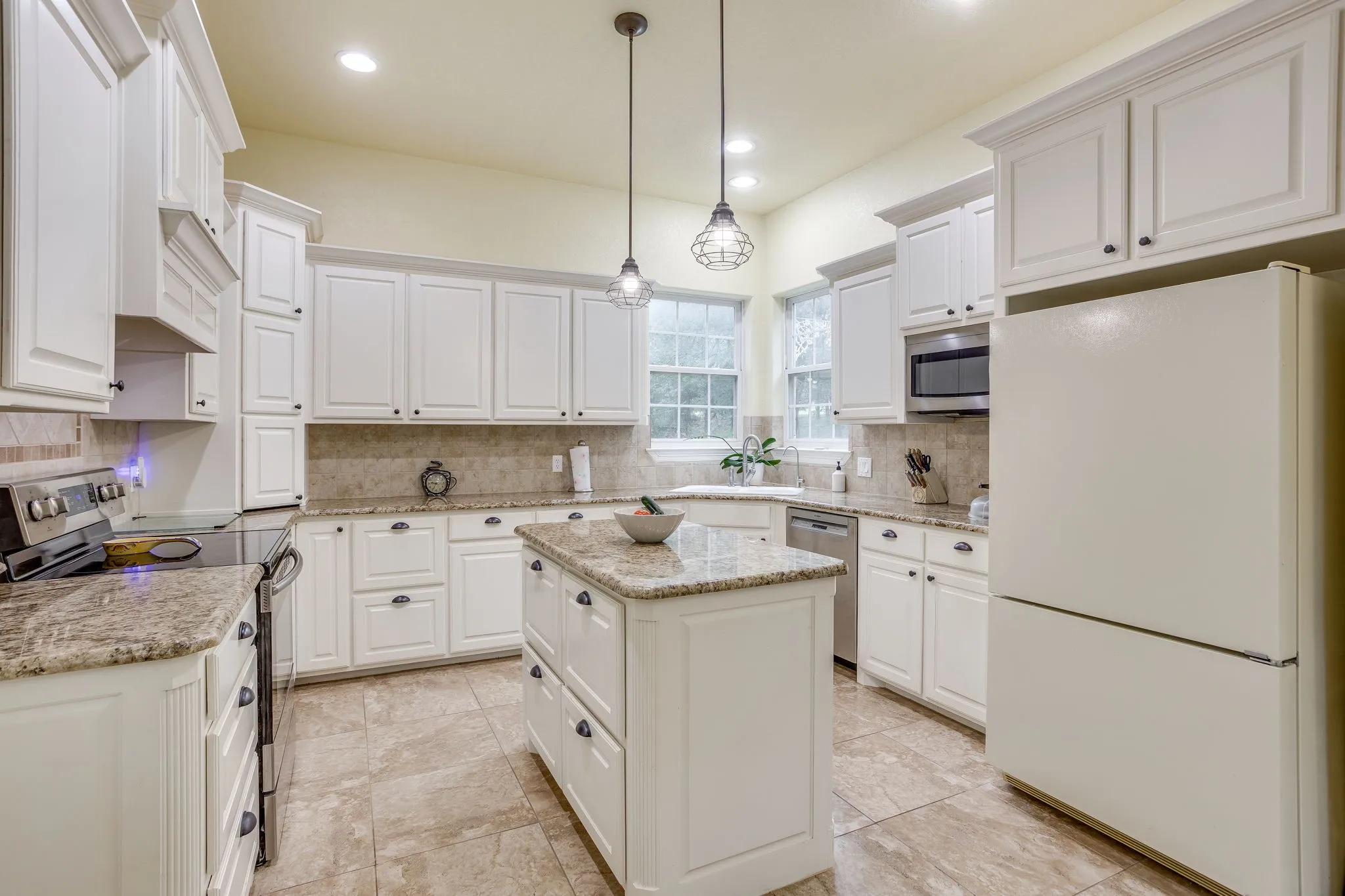 Kitchen featuring white cabinetry, granite countertops, tile backsplash, stainless steel appliances, and a central island with pendant lighting