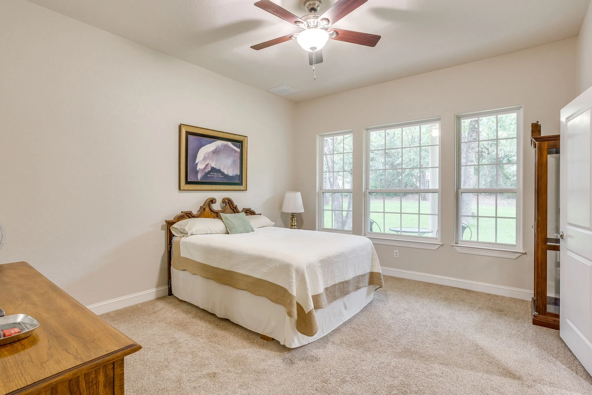 Carpeted room with three large windows overlooking mature trees