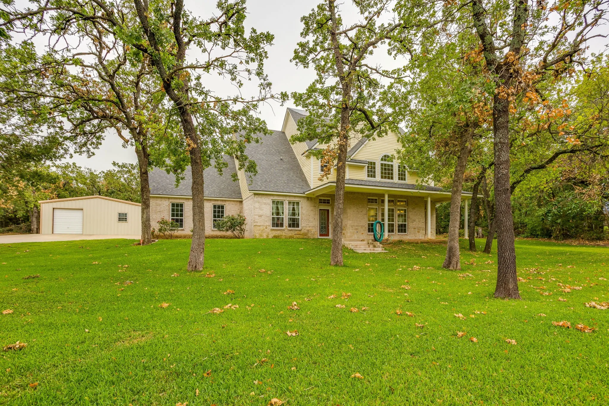 Expansive lawn and mature trees frame this residence, featuring a brick and siding exterior, a covered front porch, and multiple windows