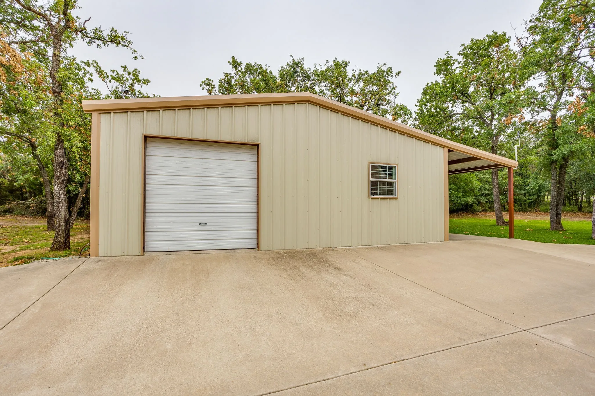 Pre-engineered metal building with a single garage door, covered carport, concrete slab foundation, and a side window