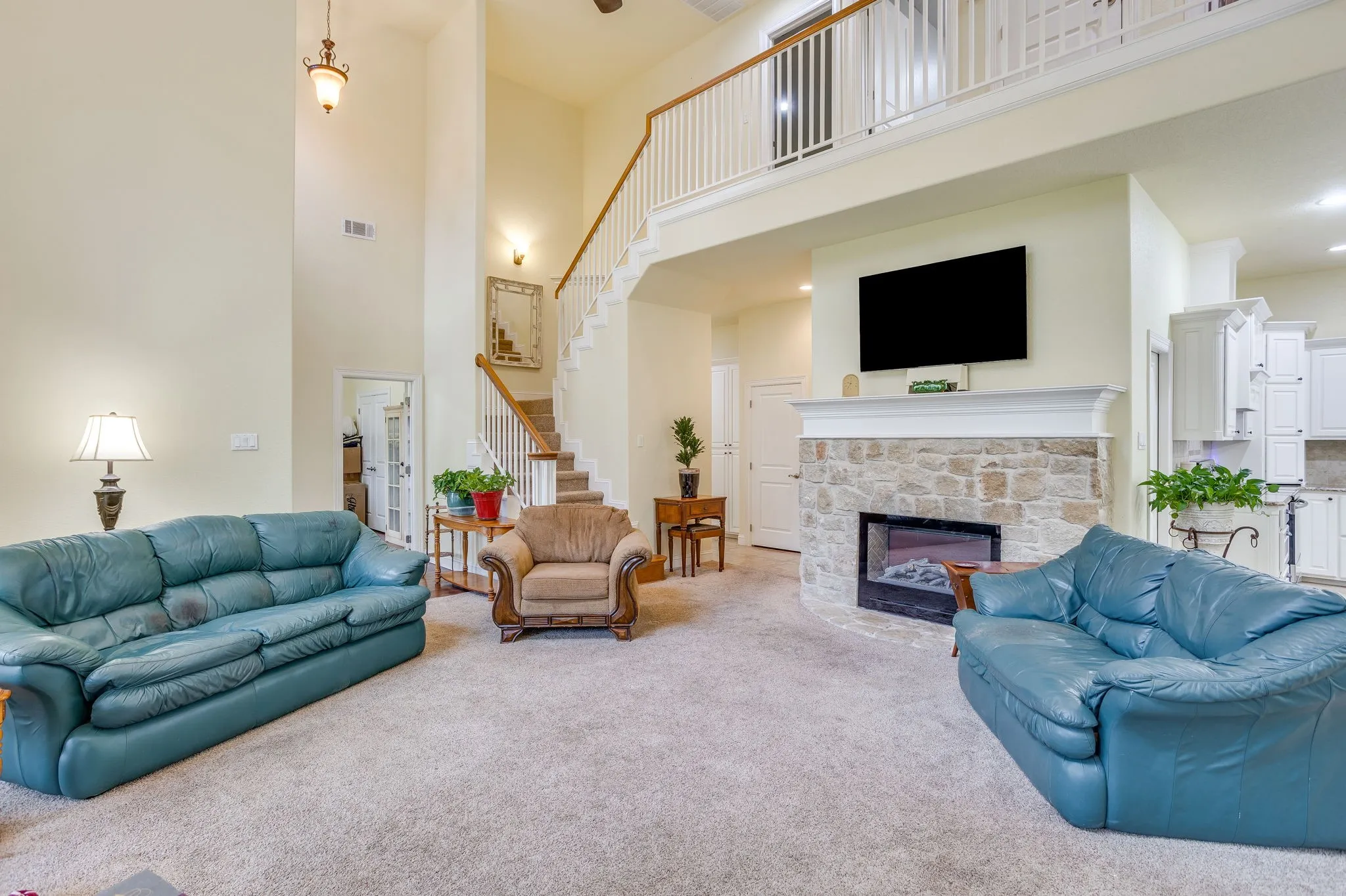 Living area featuring a stone fireplace with a substantial mantel, a two-story ceiling, and a carpeted staircase leading to a second-story landing