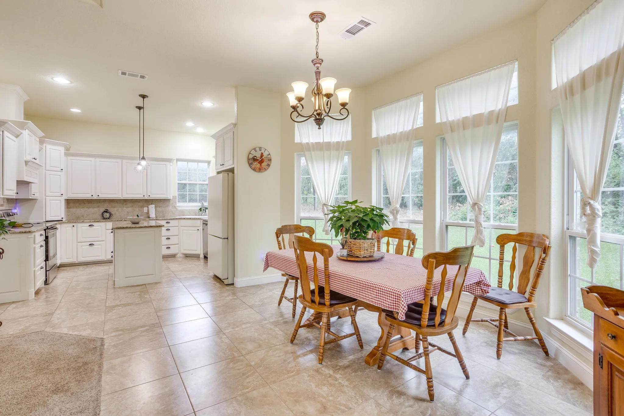 Open-concept kitchen and dining area featuring tile flooring, white cabinetry, a kitchen island with seating, a tile backsplash, and a dining area with multiple windows