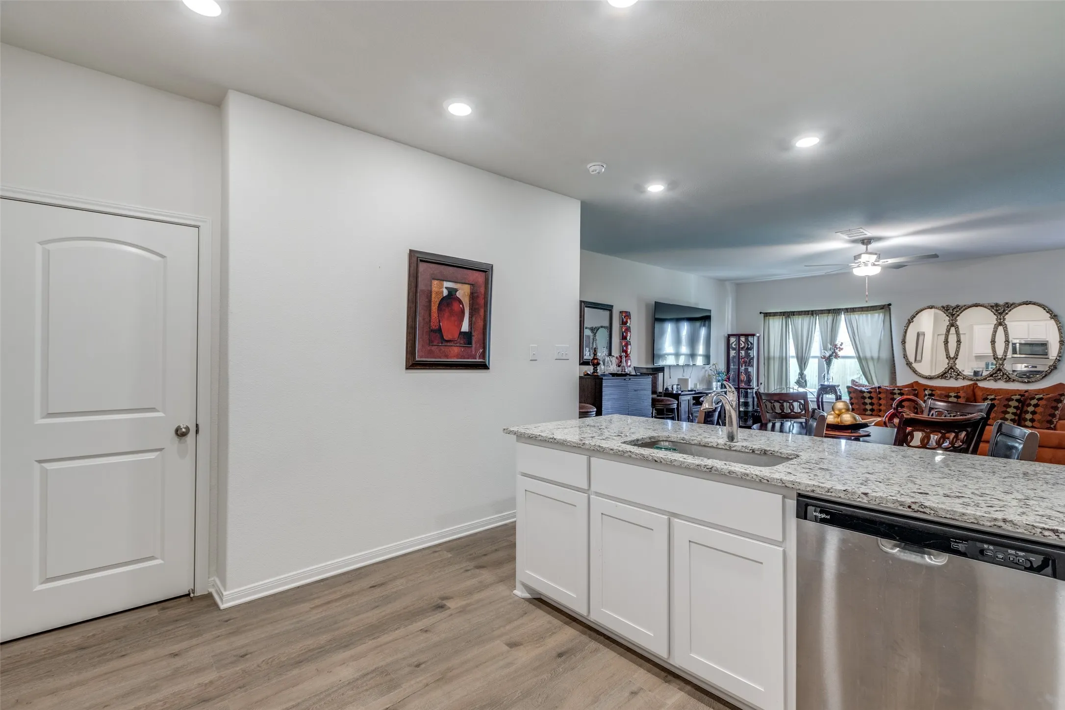 Kitchen with dishwasher, open floor plan, white cabinetry, light stone countertops, and light wood finished floors
