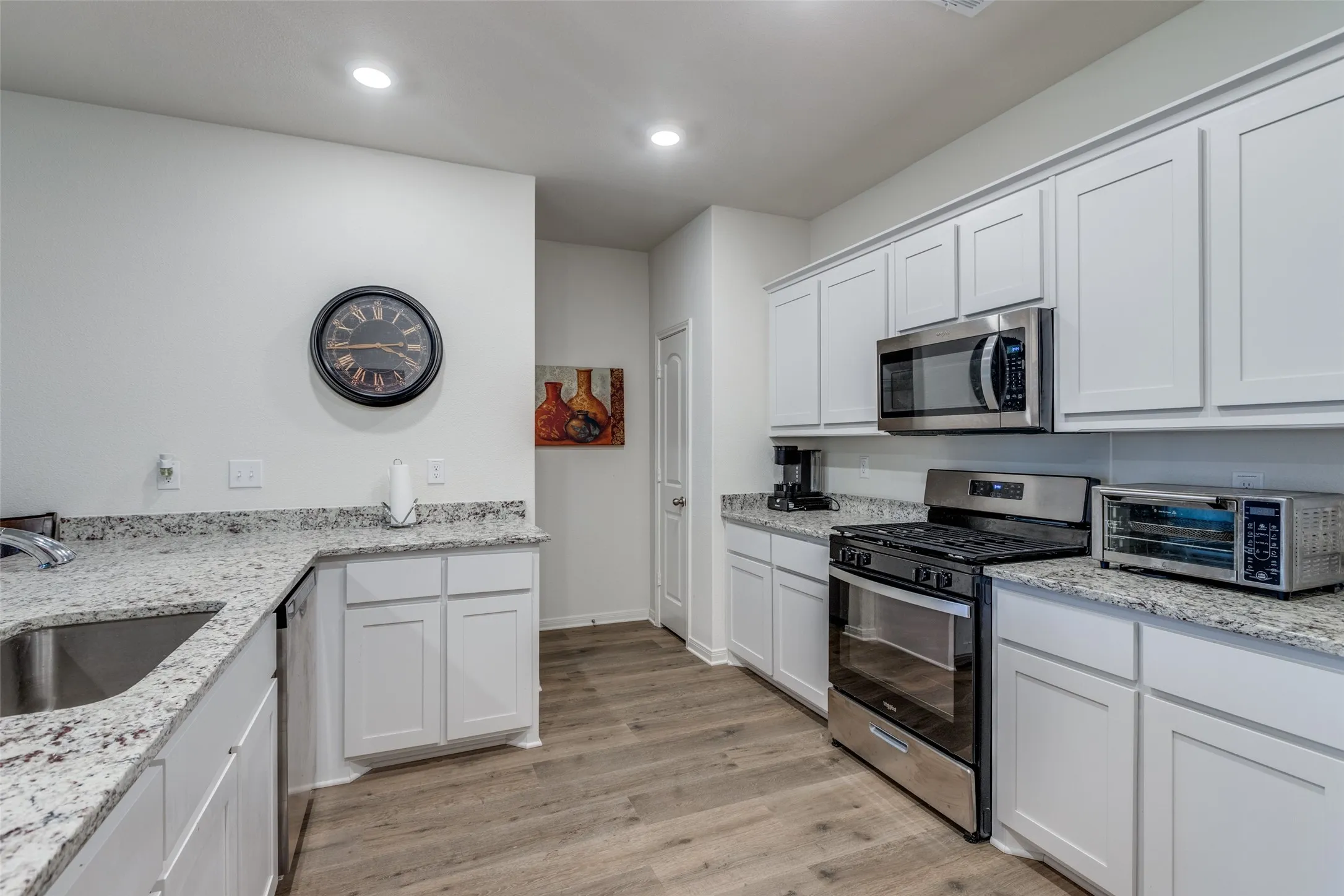 Kitchen with stainless steel appliances, light wood-type flooring, white cabinetry, light stone countertops, and recessed lighting