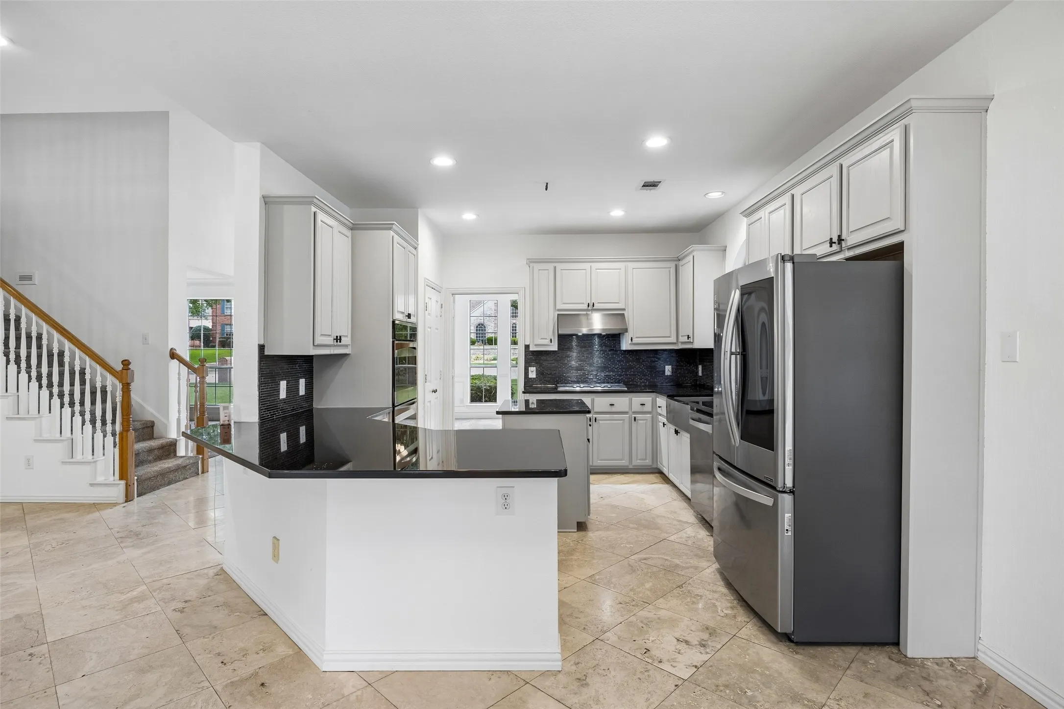 Kitchen featuring light gray cabinetry, black countertops, and a dark tile backsplash