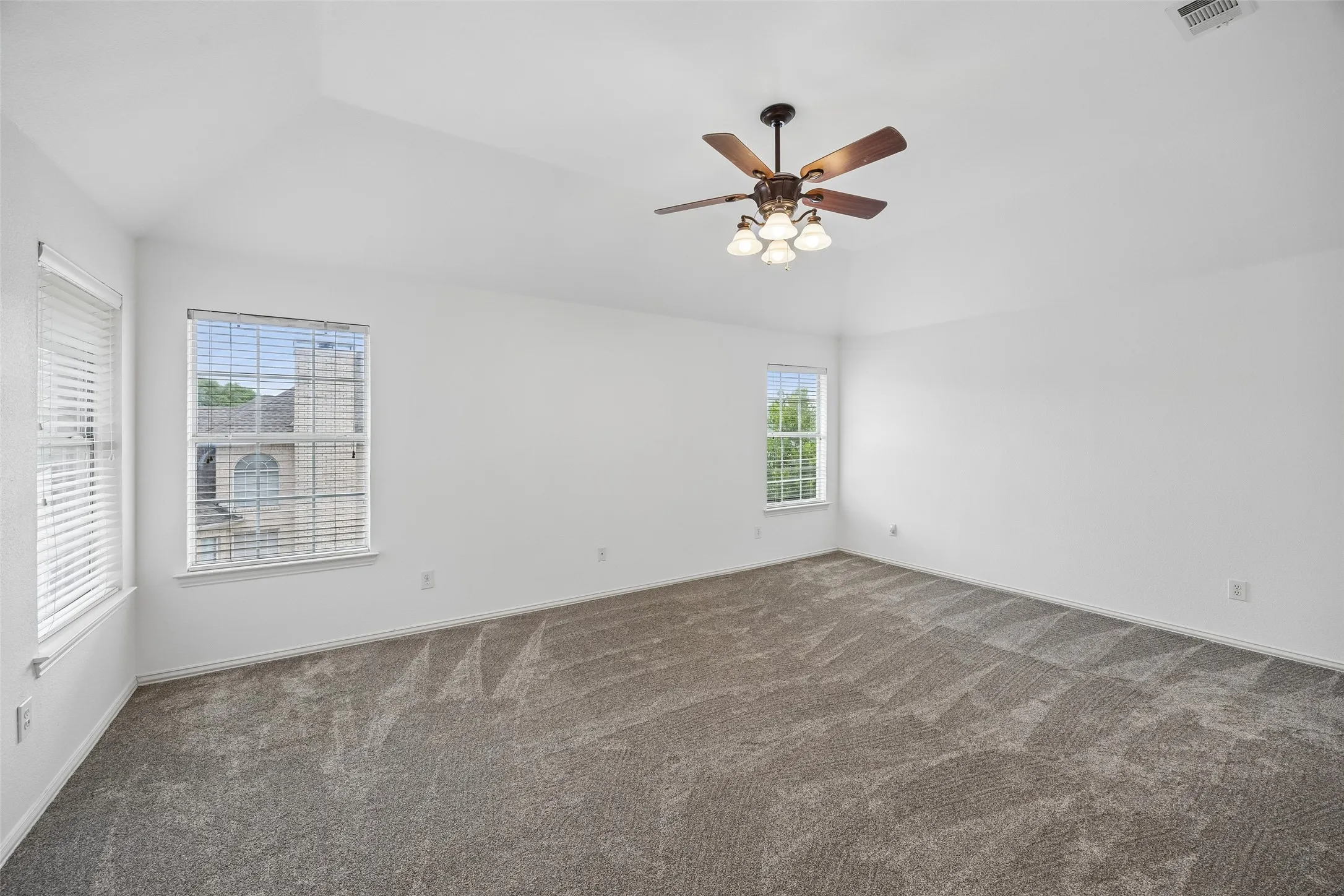 Spacious room featuring vaulted ceilings, neutral-toned carpet, multiple windows, a ceiling fan with integrated lighting, and neutral white walls