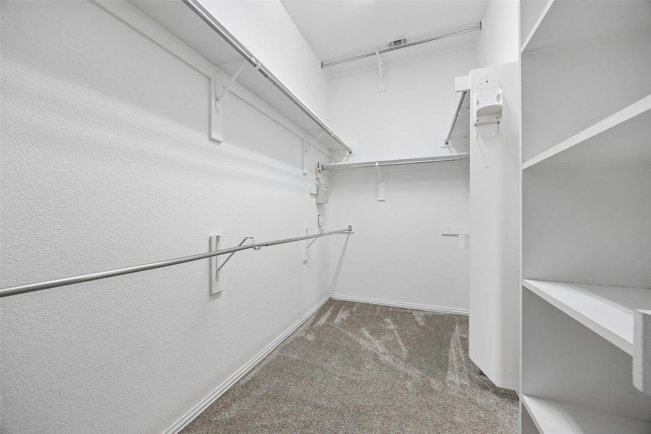 Walk-in closet featuring built-in shelving, multiple hanging rods, and neutral-toned carpeting