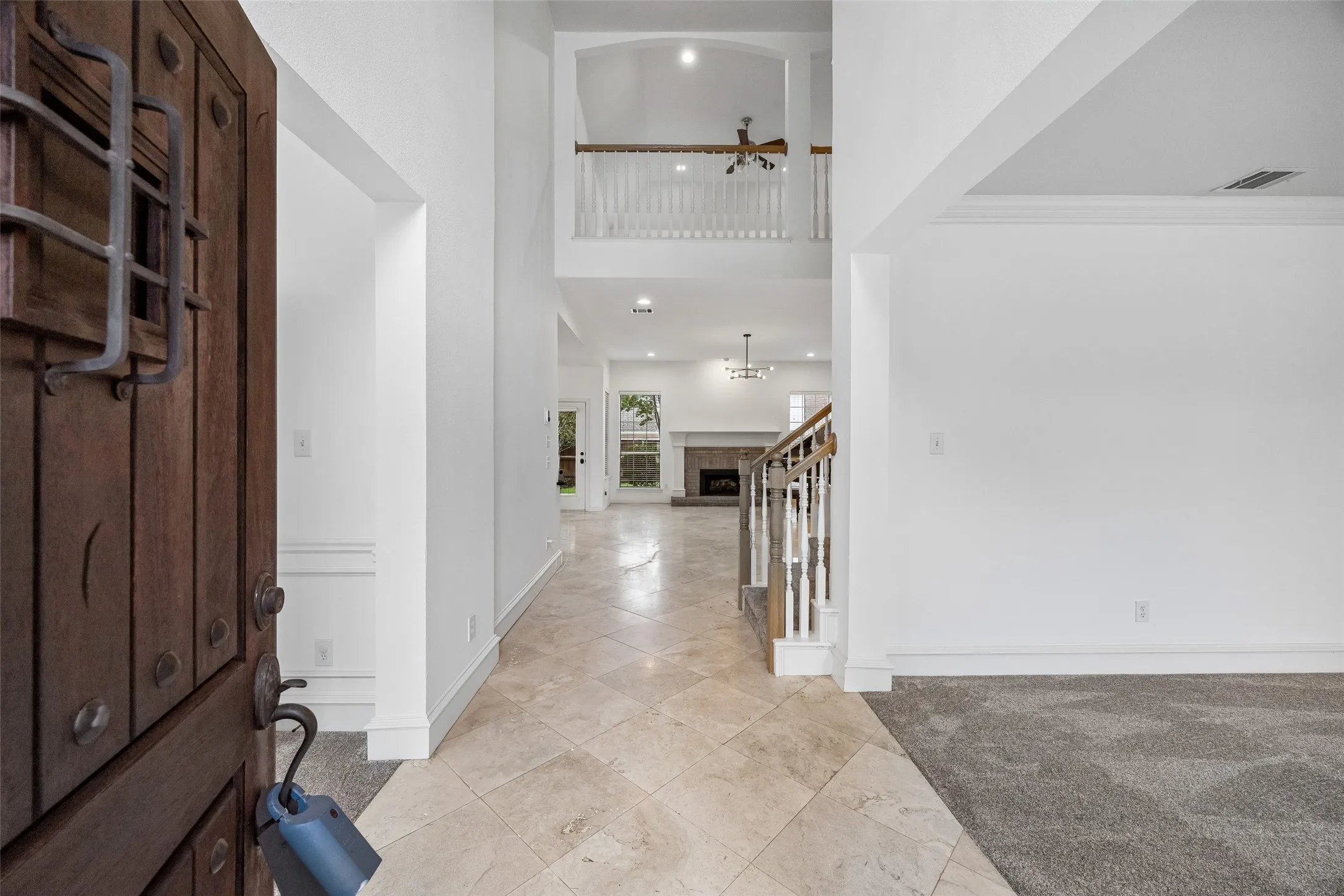 Grand entryway featuring a custom wood door with iron detailing, high ceilings, a prominent staircase with white balusters, and a spacious living area with a fireplace visible beyond