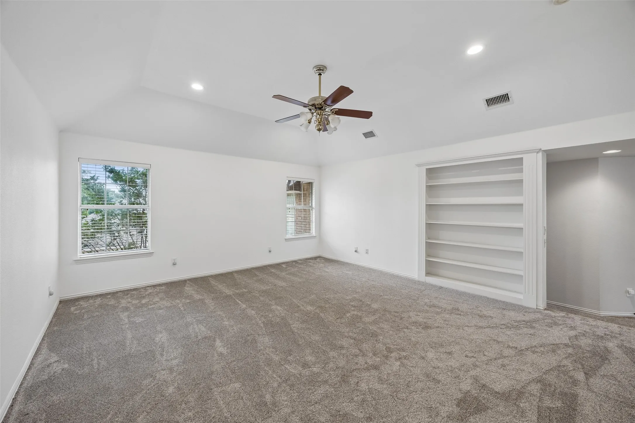 Spacious room featuring vaulted ceilings, recessed lighting, neutral-toned carpet, a ceiling fan, and built-in shelving